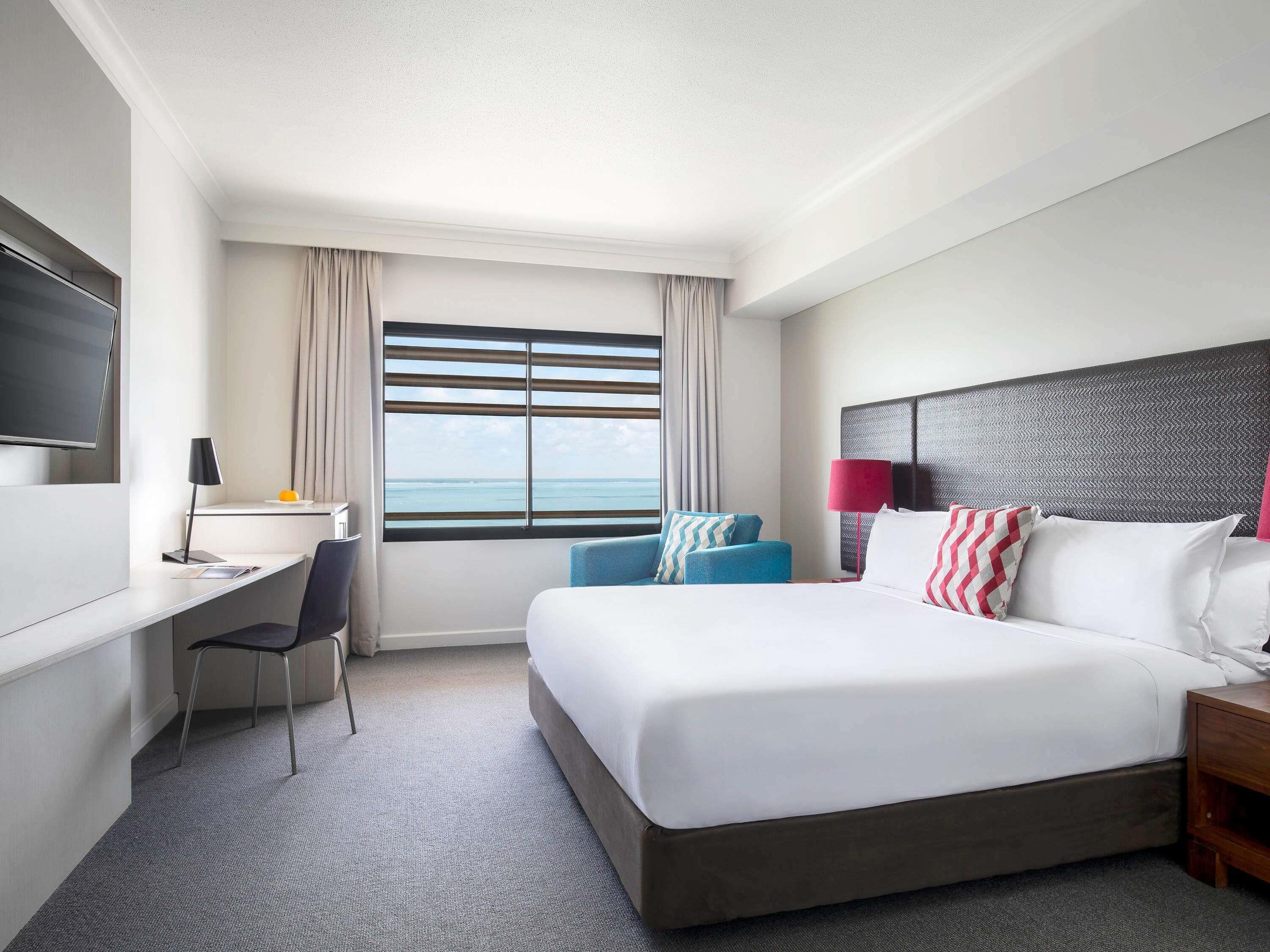A hotel room with a bed, a desk, a chair, a TV, a window with curtains, and a nightstand.