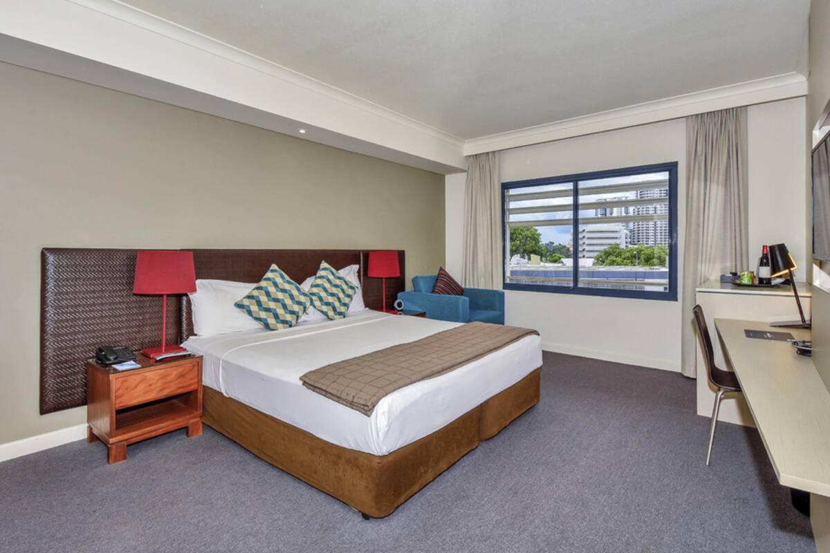 A hotel room with a large bed, bedside tables, a desk, and a window with a view.