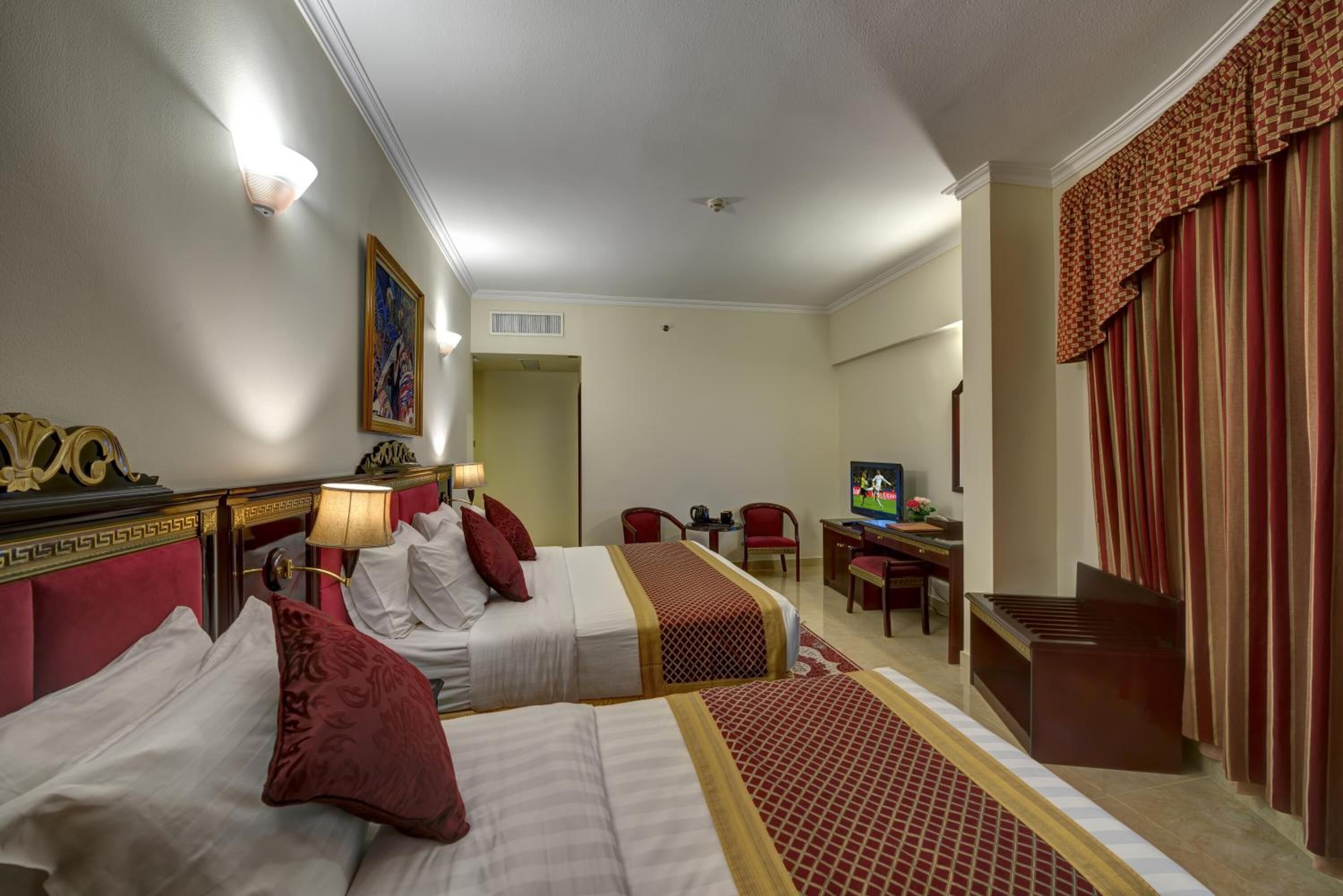 A hotel room with two beds, a desk, a television, and a window with curtains.