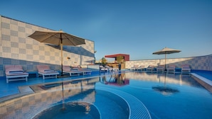 A swimming pool with lounge chairs and umbrellas, surrounded by a tiled wall.
