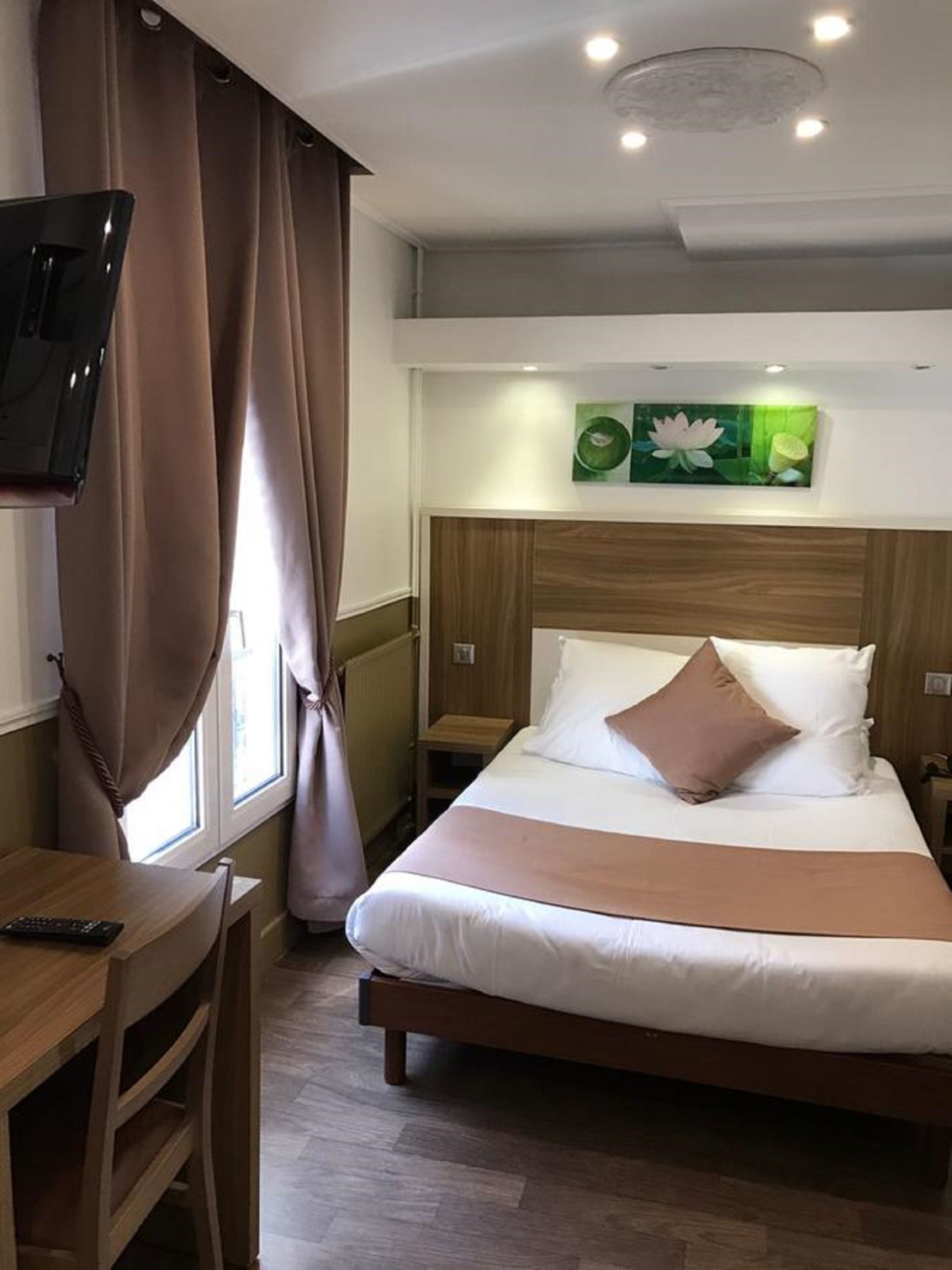 A hotel room with a bed, a TV, a desk, and a window with curtains.