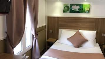 Una habitación de hotel con cama, televisión, escritorio y ventana con cortinas.