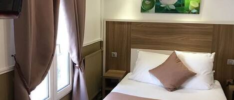 A hotel room with a bed, a TV, a desk, and a window with curtains.