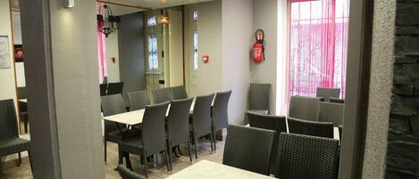 Un restaurant avec plusieurs tables et chaises, un extincteur accroché au mur et une fenêtre ornée d’un rideau rouge.