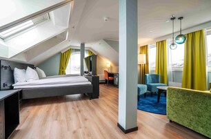 A modern hotel room with a loft bed, a desk, a chair, a sofa, and a dining table.