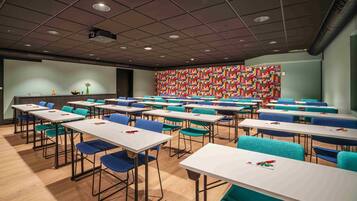 Un salón de conferencias con varias mesas y sillas, un proyector en el techo y un diseño de pared geométrico y colorido.