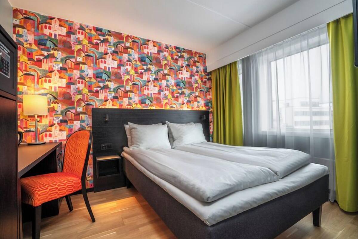 Une chambre d’hôtel avec un lit, un bureau, une chaise, une table de chevet et un mur aux couleurs vives.