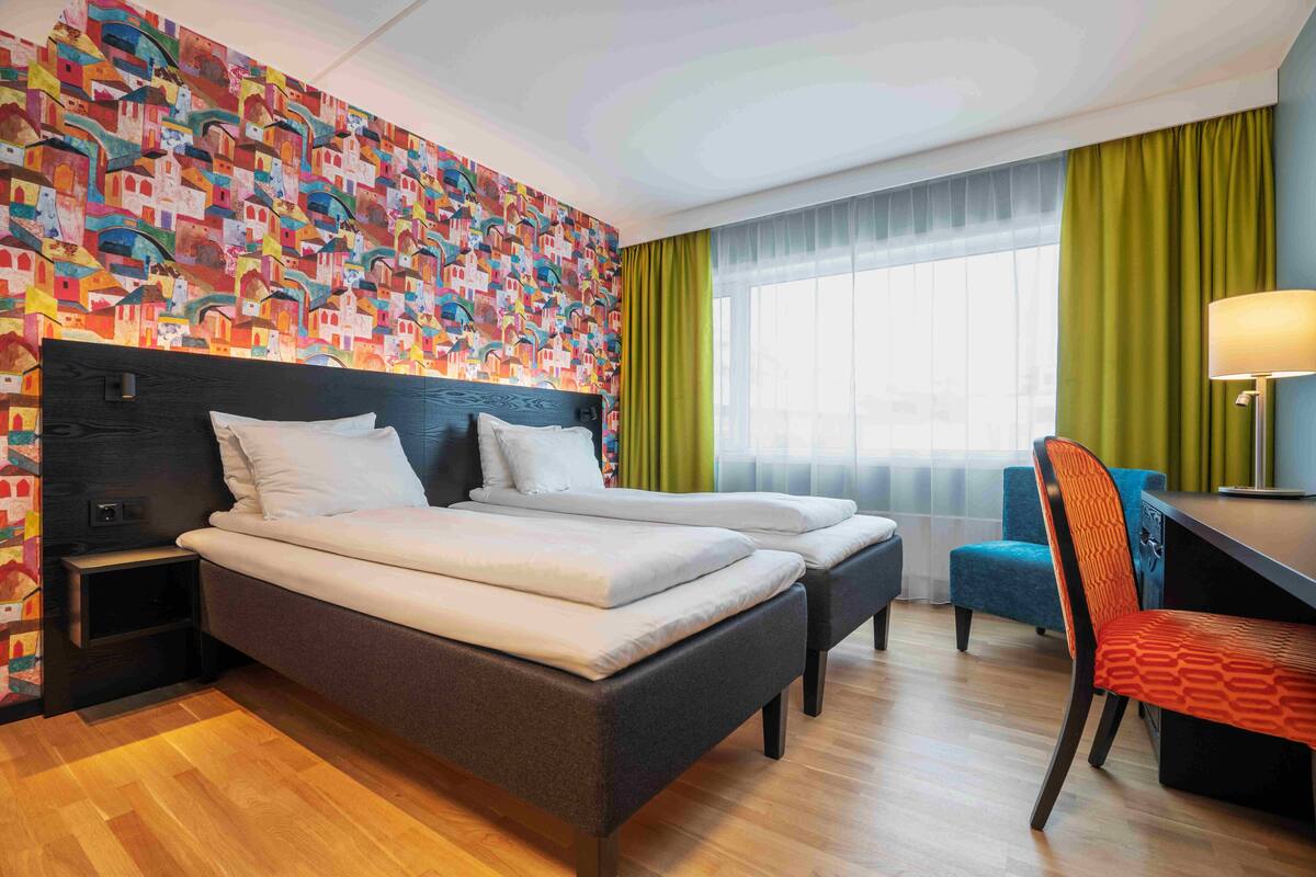 Une chambre d’hôtel avec un grand lit, un bureau, une chaise et une fresque colorée sur le mur.