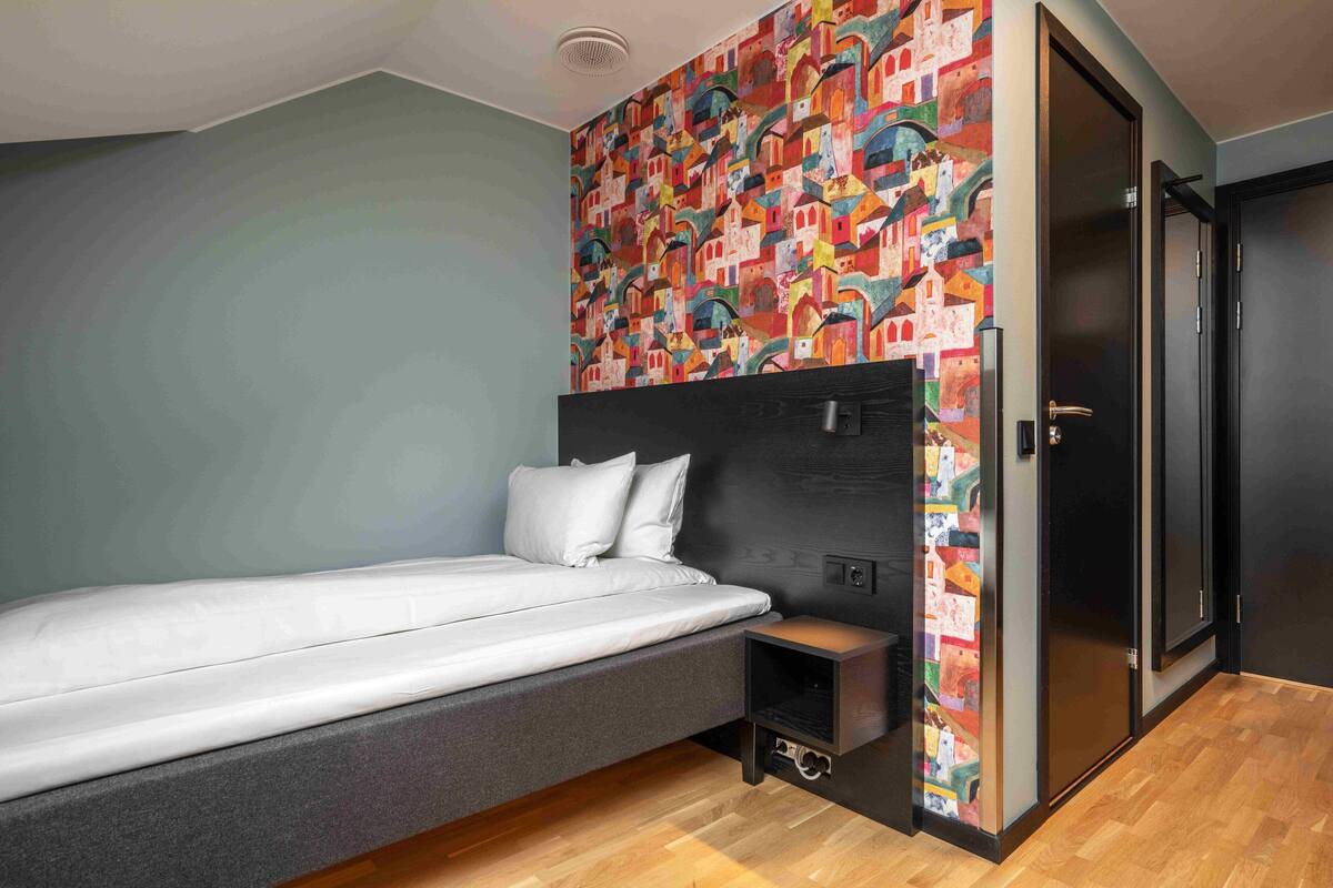 Une chambre moderne avec un lit, une tête de lit ornée d’une fresque colorée, un plancher en bois et une porte.