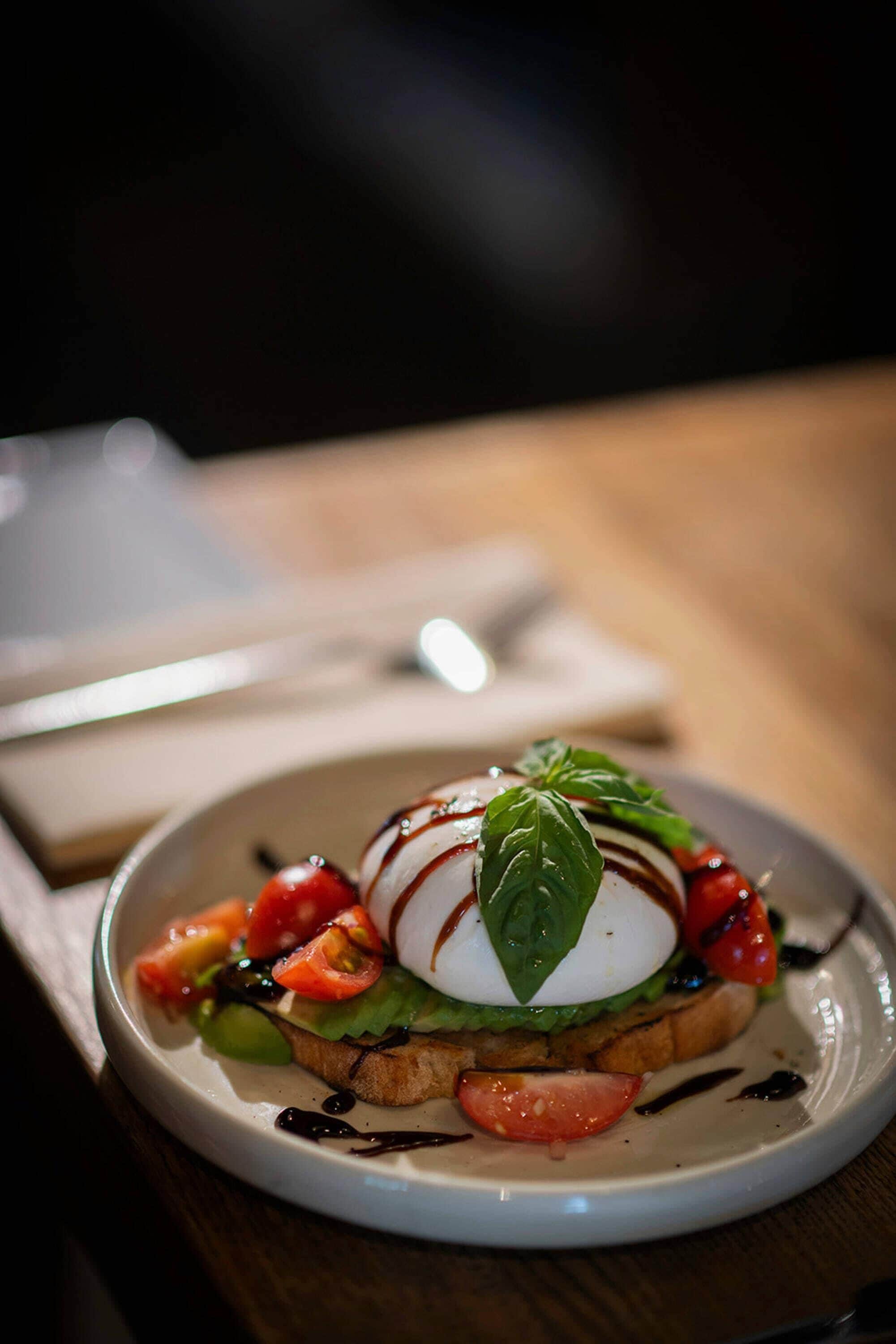 A plate with a sandwich topped with a slice of tomato, a leaf, and a drizzle of sauce.