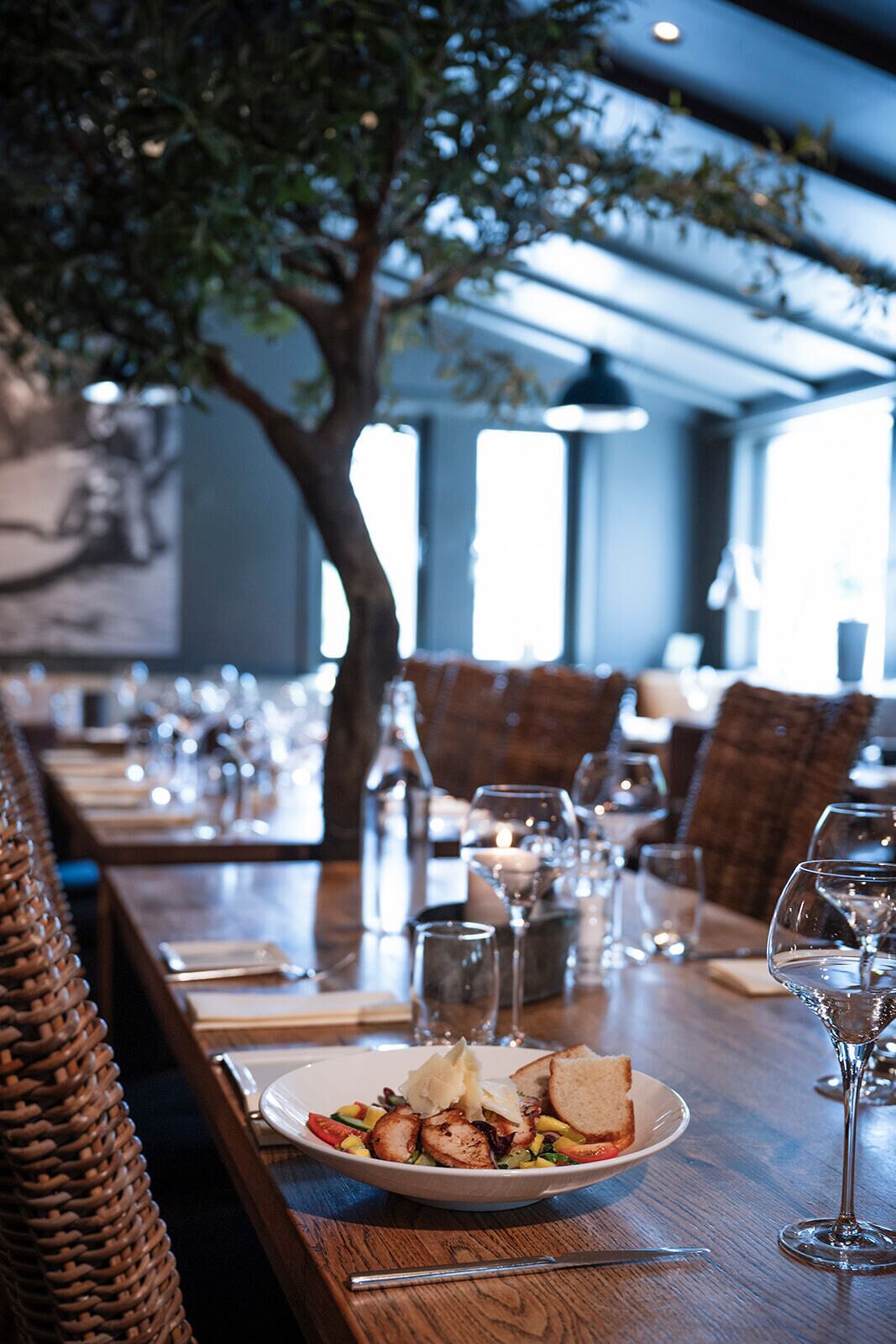 Un ambiente de restaurante con una mesa para dos, que incluye un plato de comida, copas de vino y una vela.