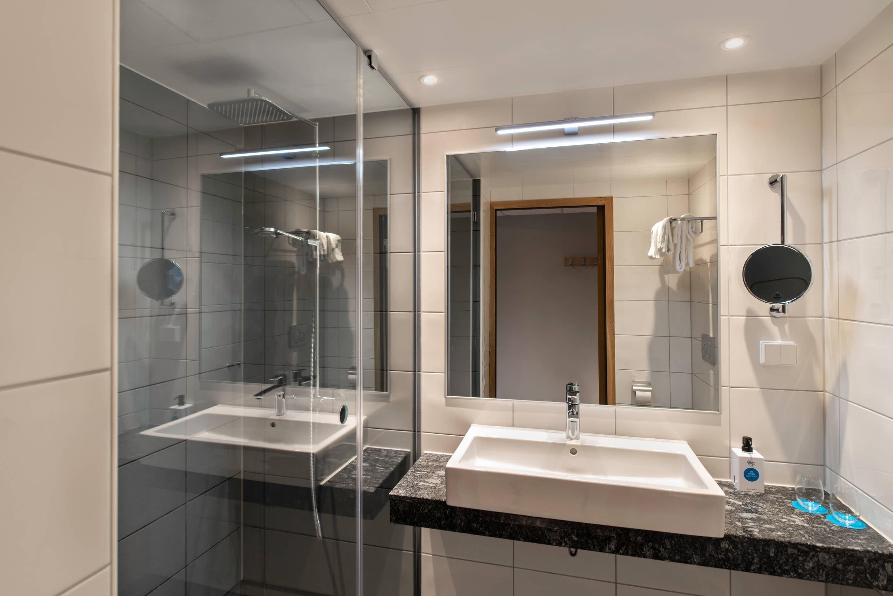Un baño moderno con dos lavamanos, un box de ducha de vidrio y un espejo grande.