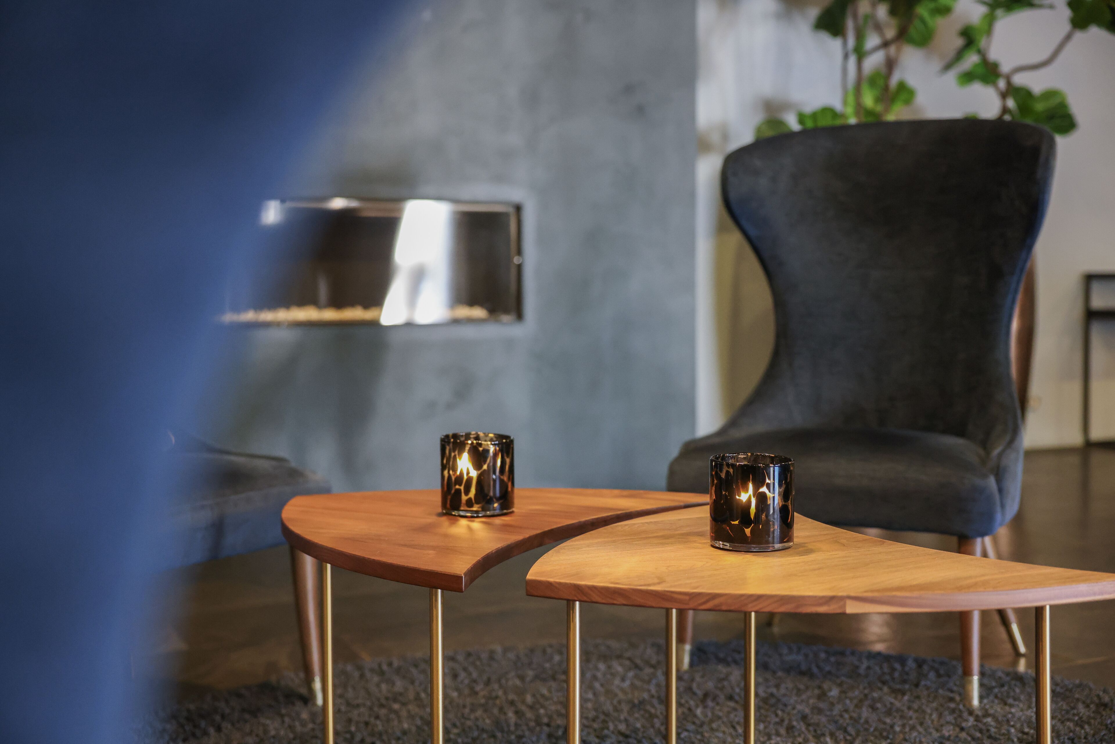 A modern living room with a curved wooden coffee table, two decorative glass vases, a dark upholstered armchair, and a built-in fireplace.