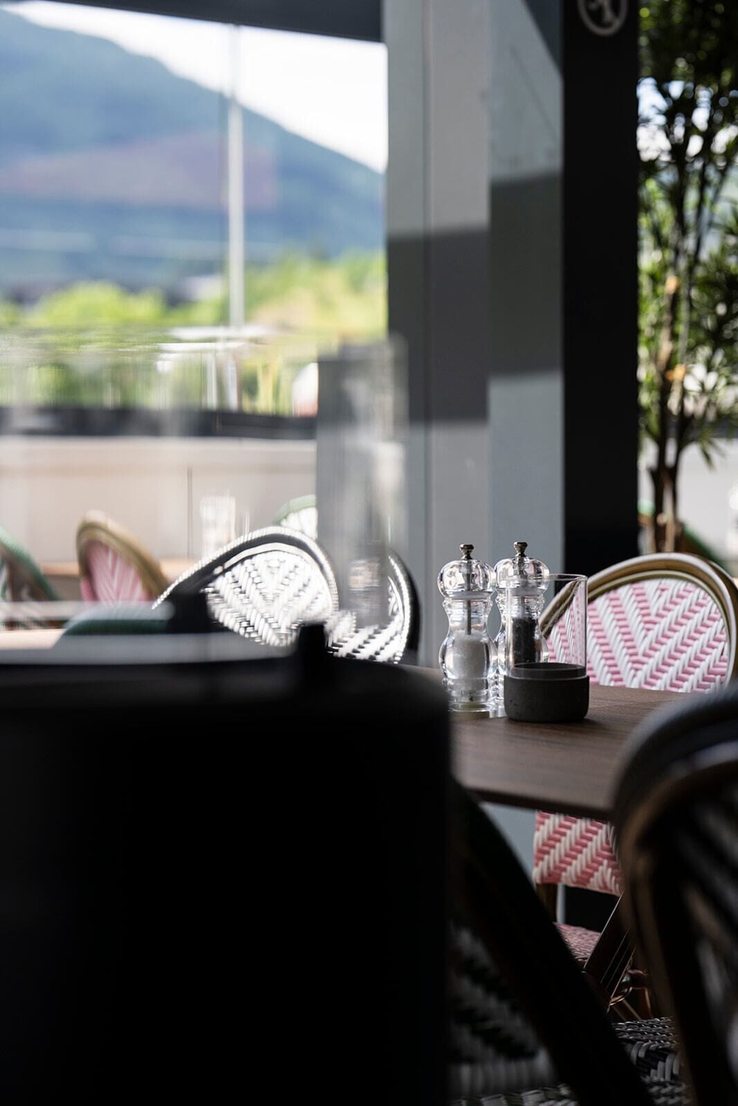 A table with salt and pepper shakers, a glass, and a black object, likely a napkin holder, in a room with wicker chairs and a view of mountains through a window.