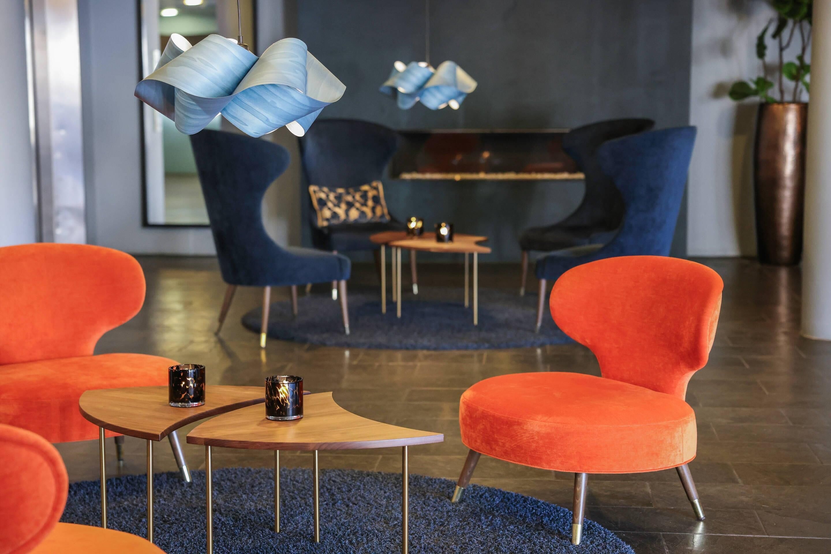 A modern lounge area with blue and orange chairs, a wooden coffee table, and decorative lamps.