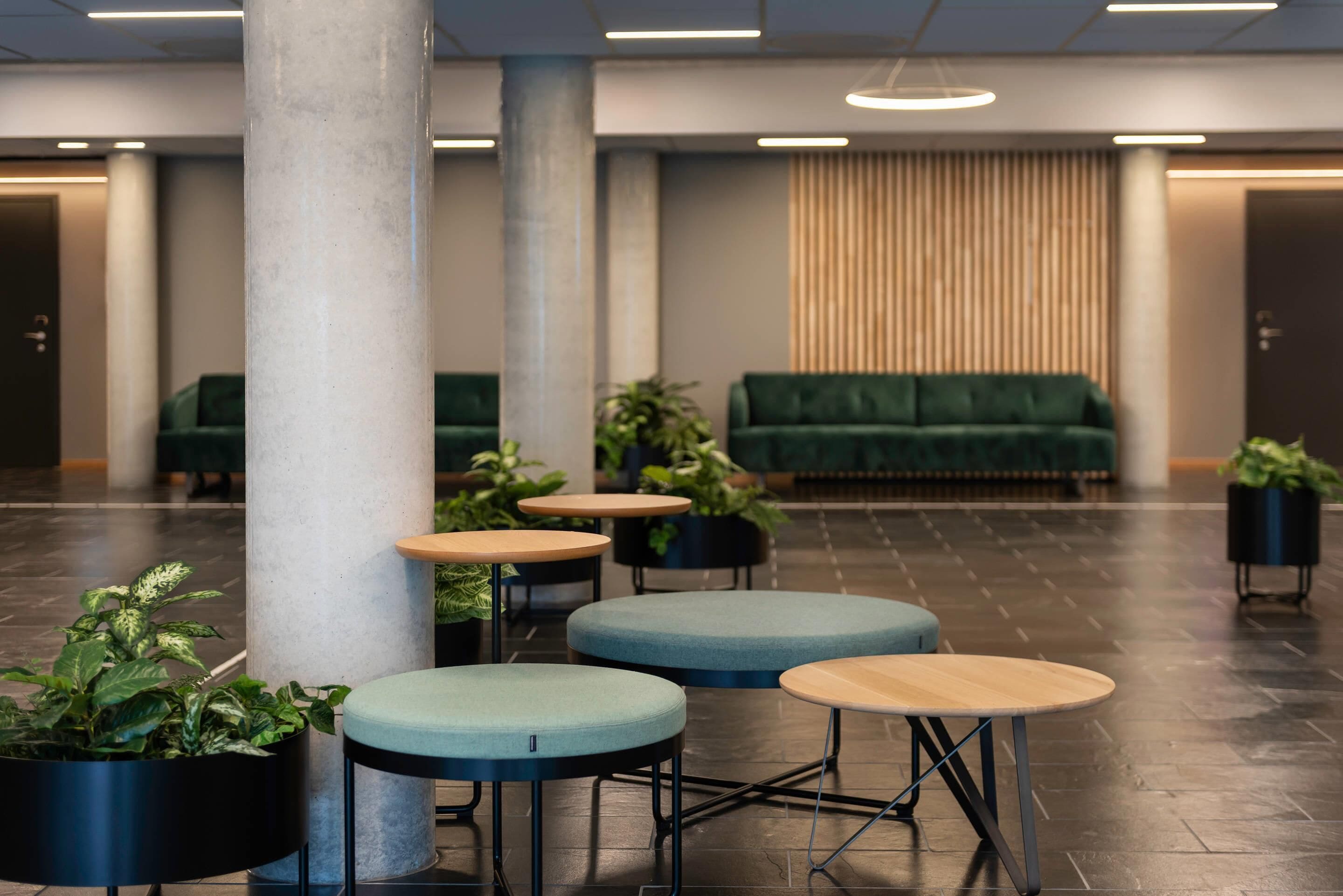 A modern lobby with a green sofa, round tables, and potted plants.