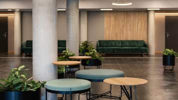 A modern lobby with a green sofa, round tables, and potted plants.