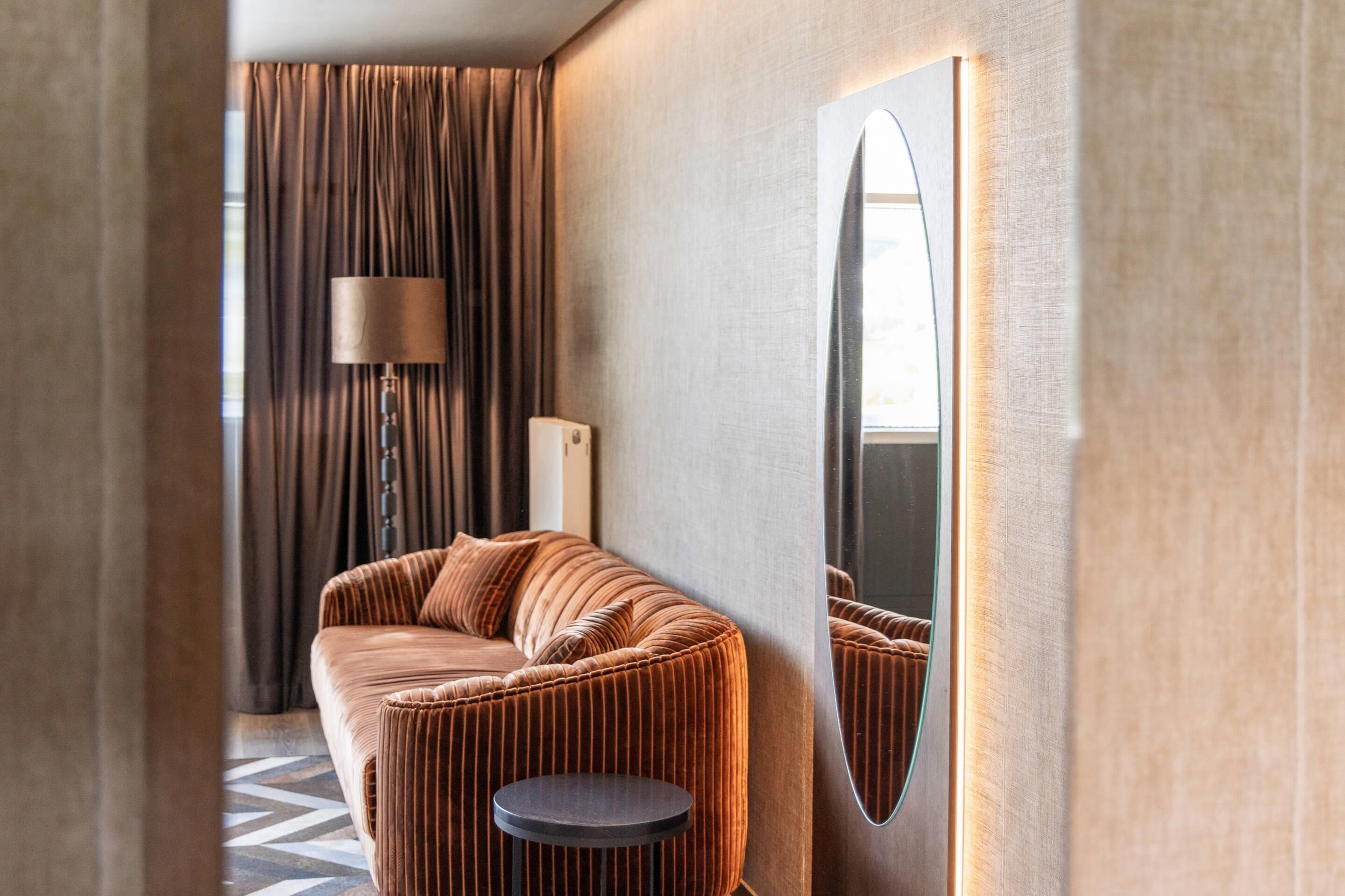 A modern room with a curved sofa, a round side table, a floor lamp, and a large mirror.