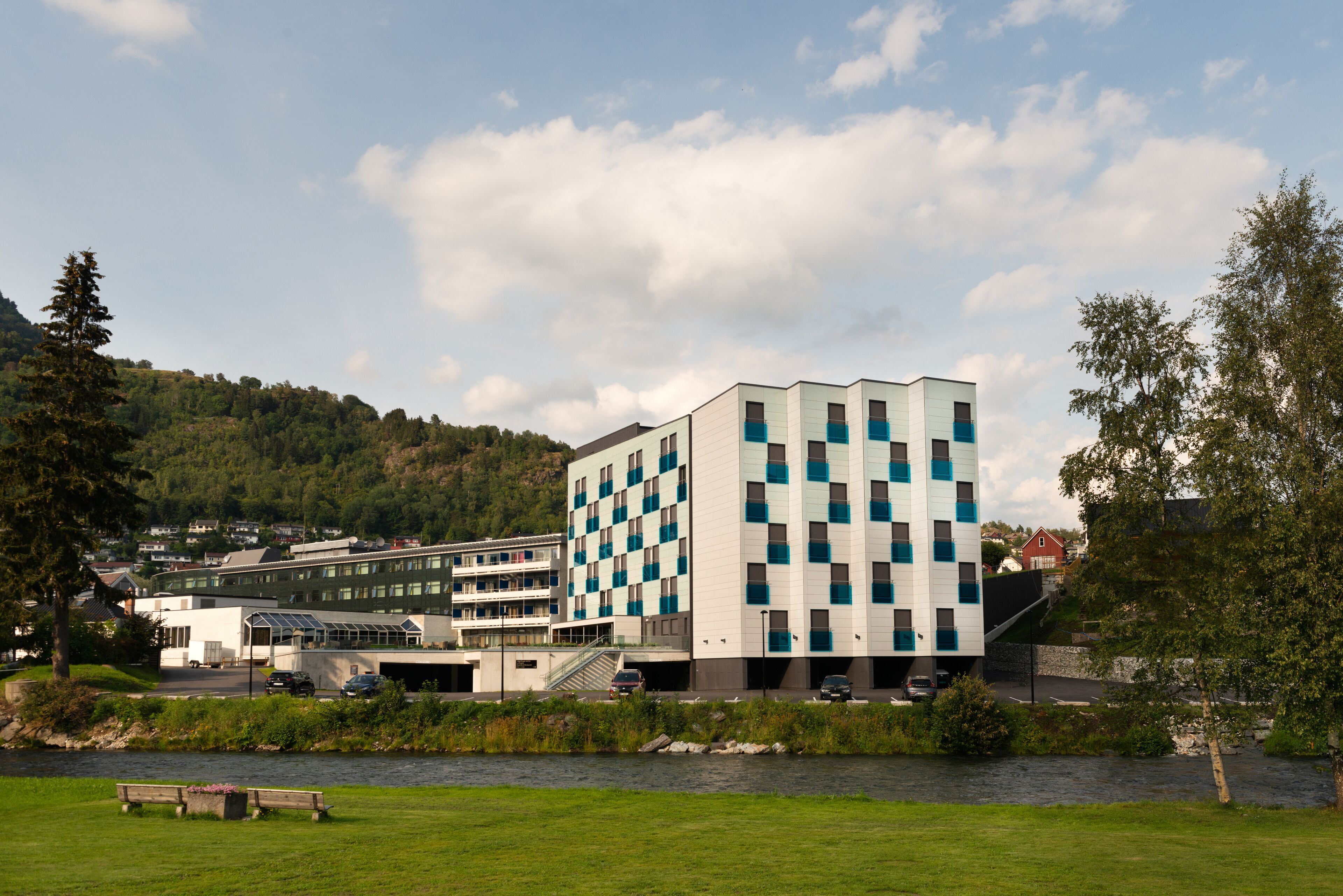 A modern building with a checkered facade, a parking area, and a river in the foreground.