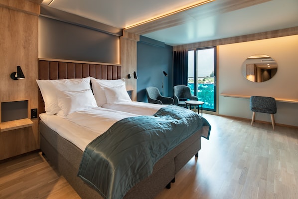 A modern hotel room with a large bed, a seating area with two chairs, a small table, and a large window offering a view. - Quality Hotel Sogndal (Sogndal)