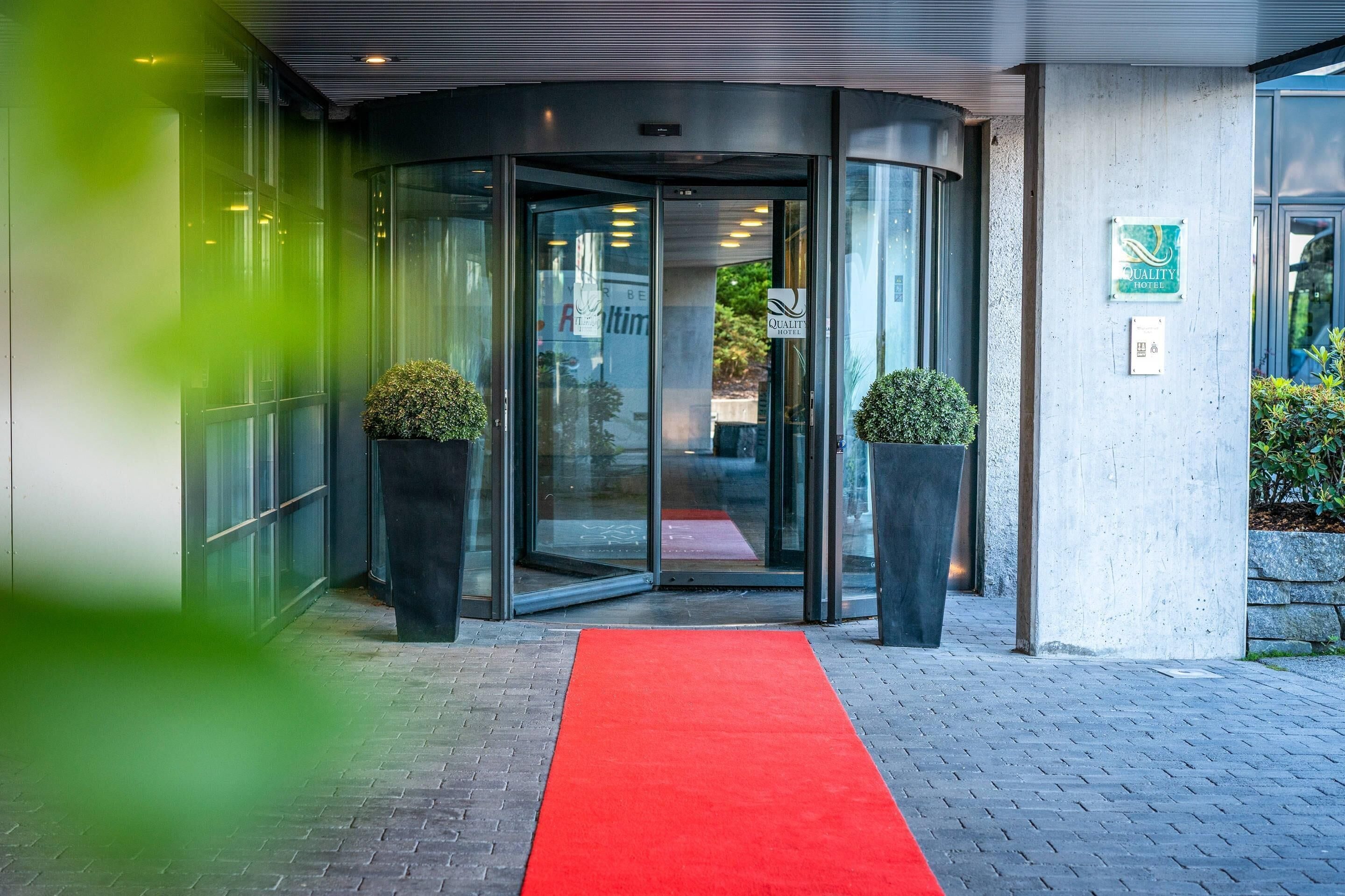 En hotelindgang med en drejeindgang, rød løber og to plantekasser.