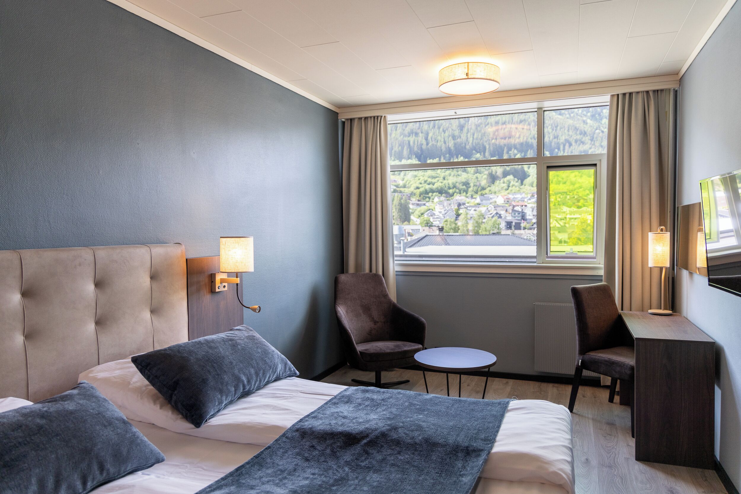 A hotel room with a large bed, two armchairs, a small table, and a TV.