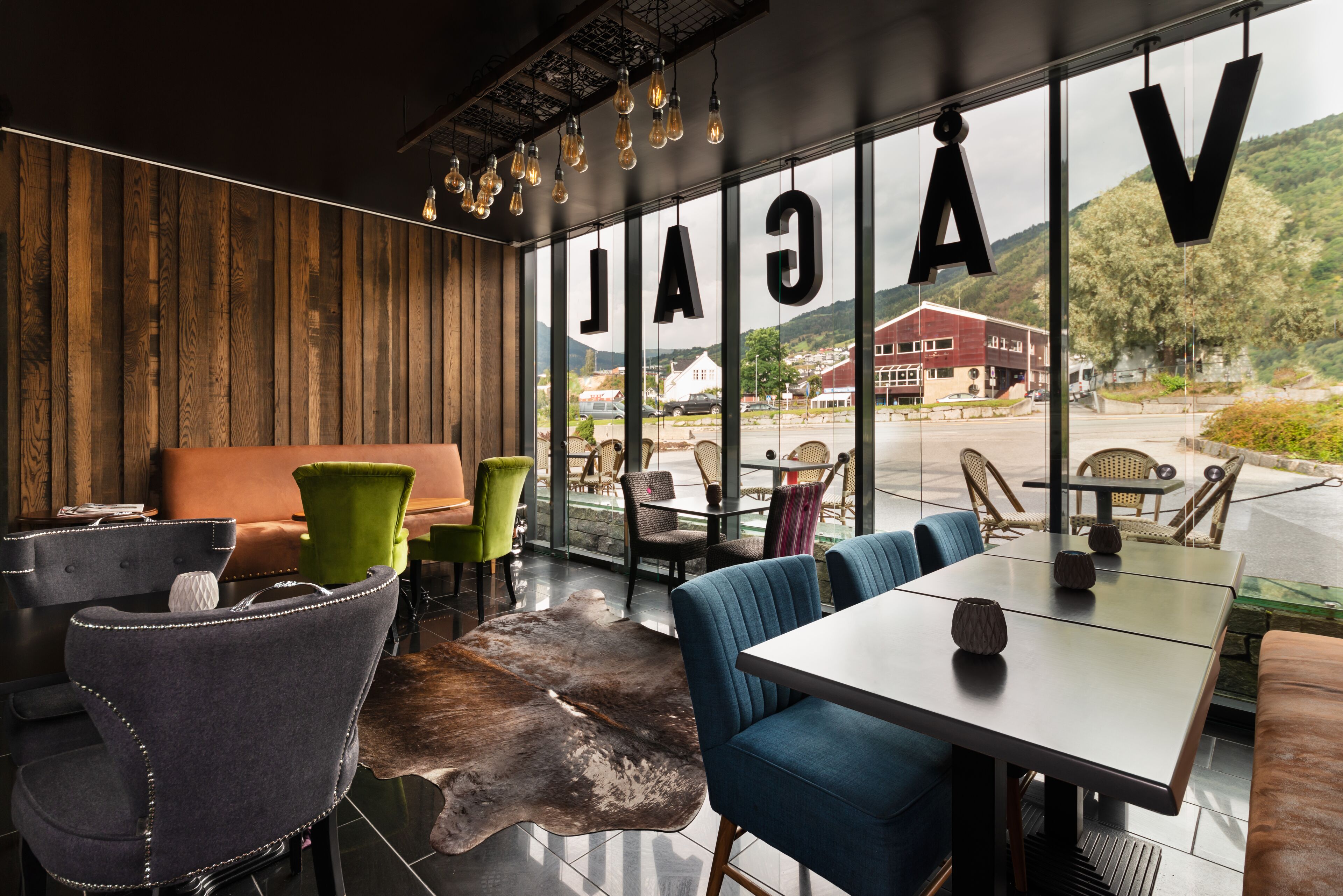 A modern interior with a wooden wall, leather seating, and a view of a building and mountains.