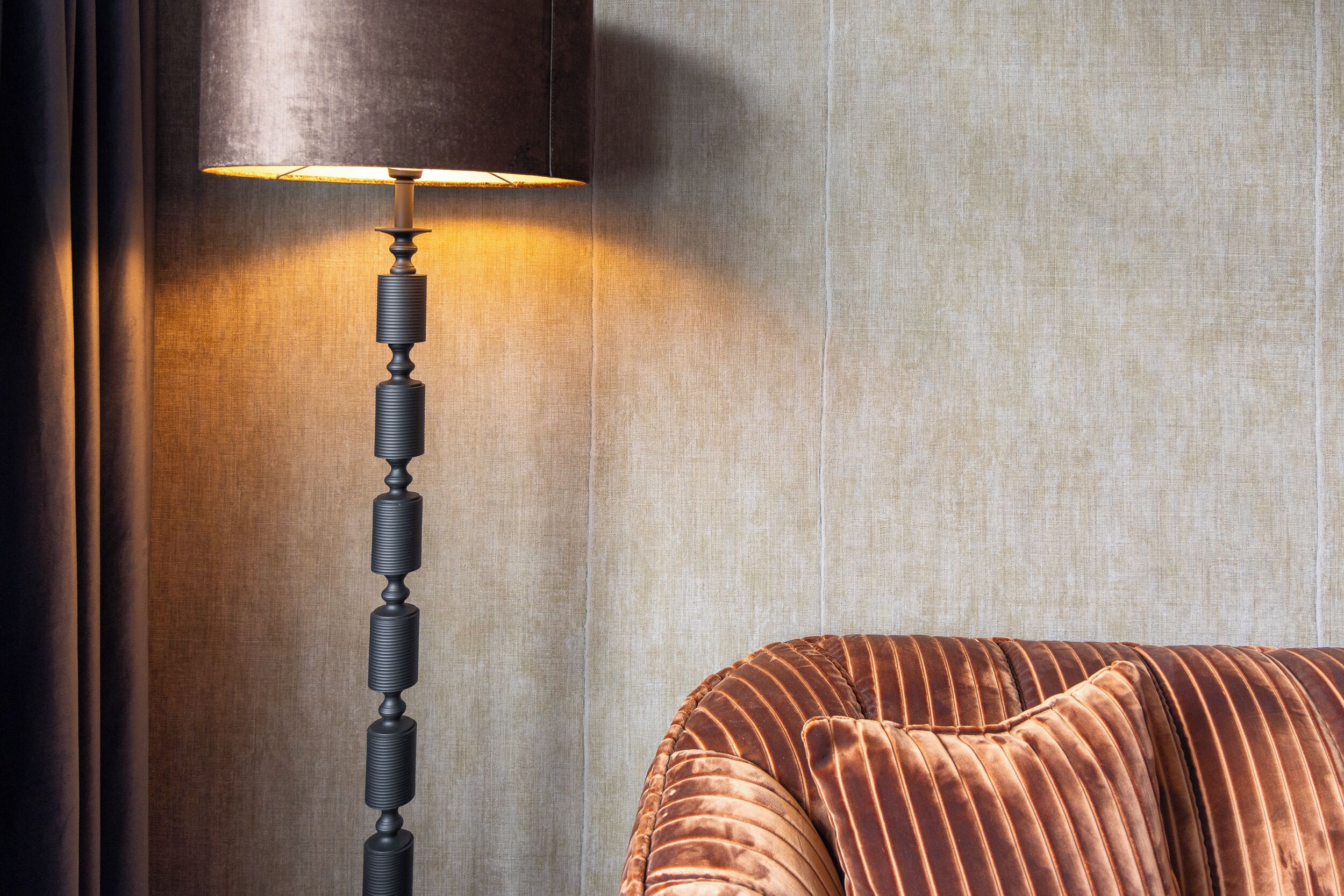 A lamp with a dark shade and a textured stand, positioned next to a cushioned seating area with a striped pattern.