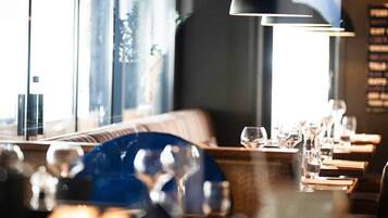 Interior de un restaurante con una larga mesa de comedor, iluminación colgante y ventanas amplias.
