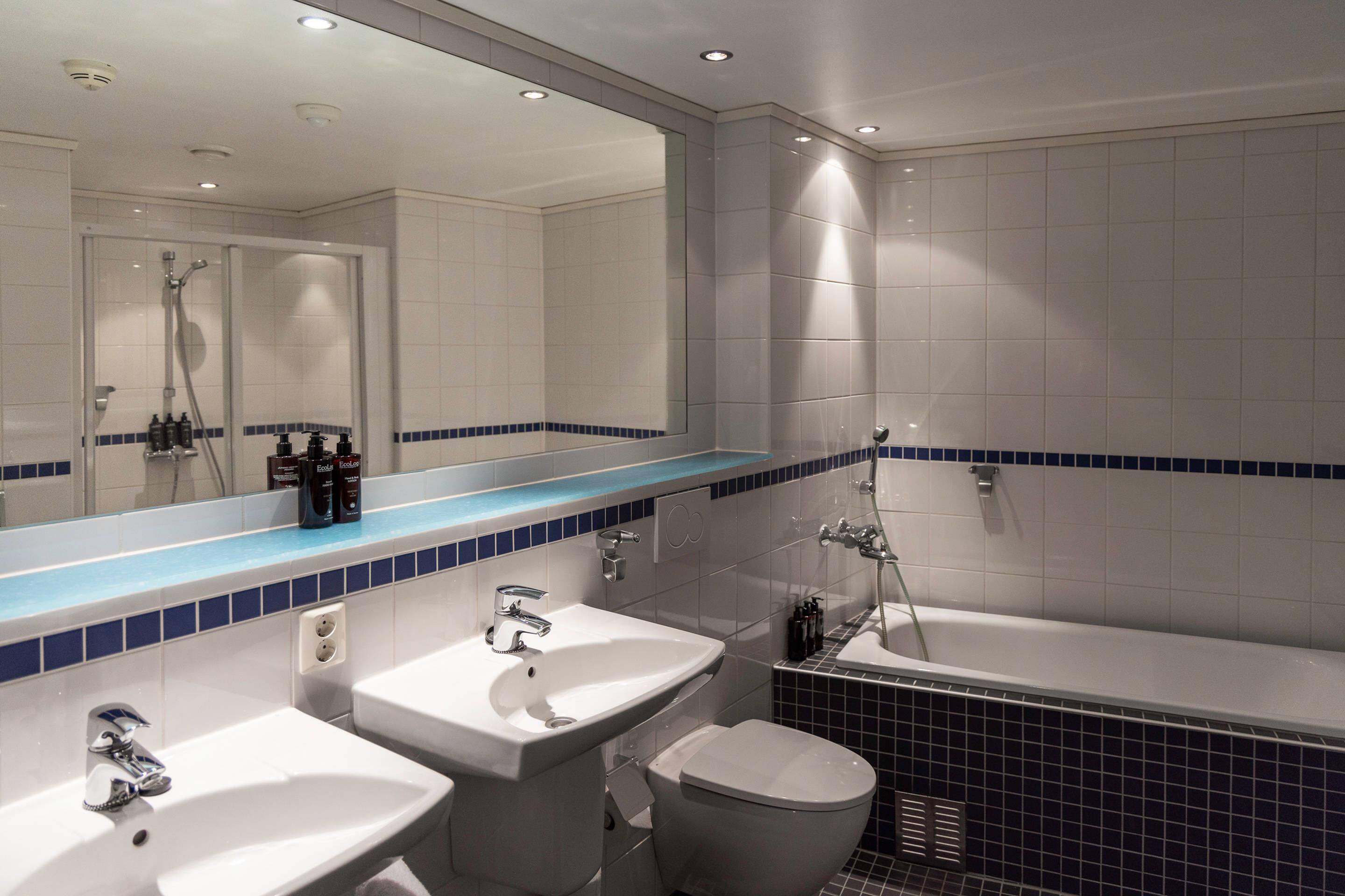 A modern bathroom with a large mirror, two sinks, a toilet, and a bathtub.