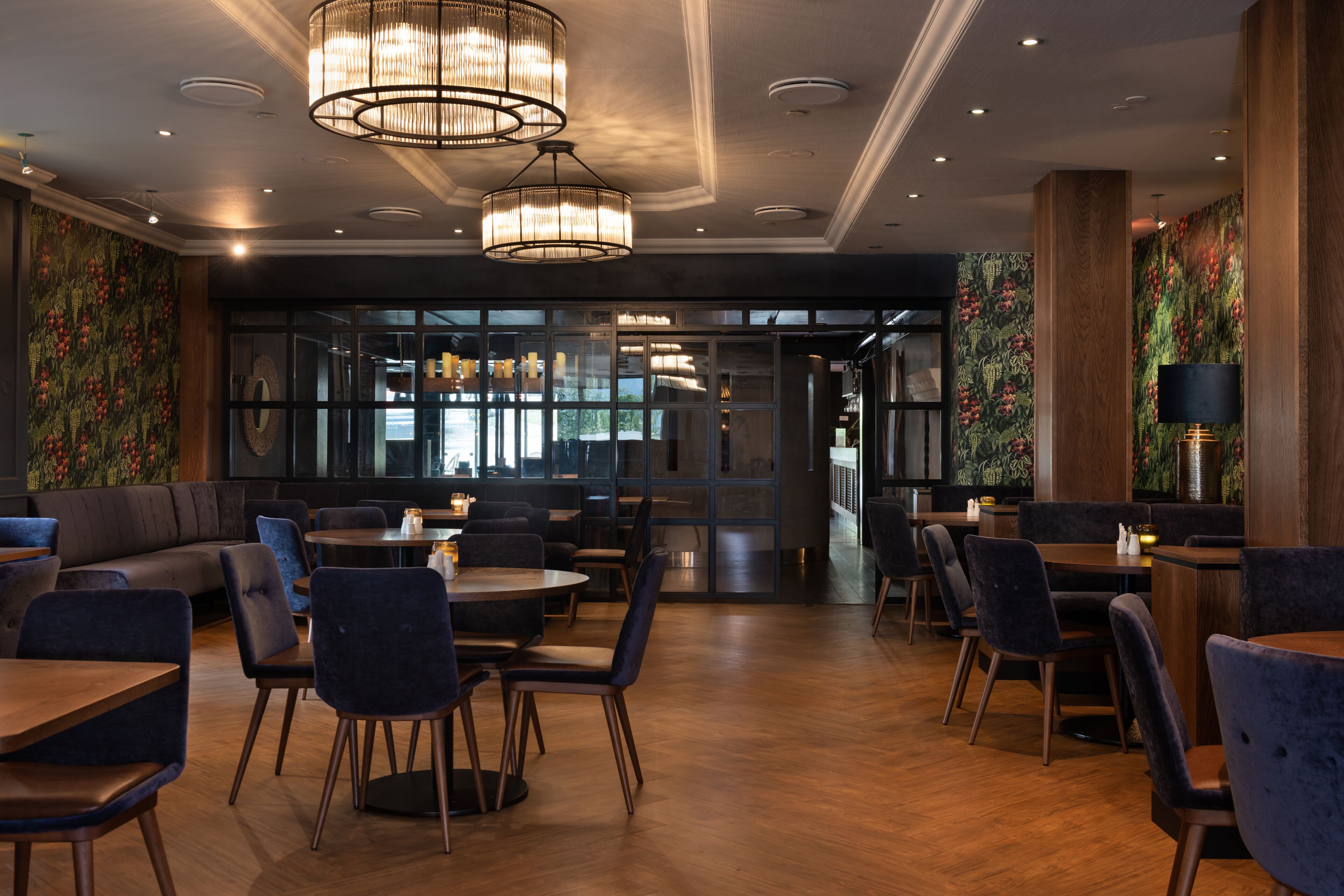 Interior de restaurante moderno com soalho de madeira, cadeiras estofadas em azul escuro e um lustre grande.