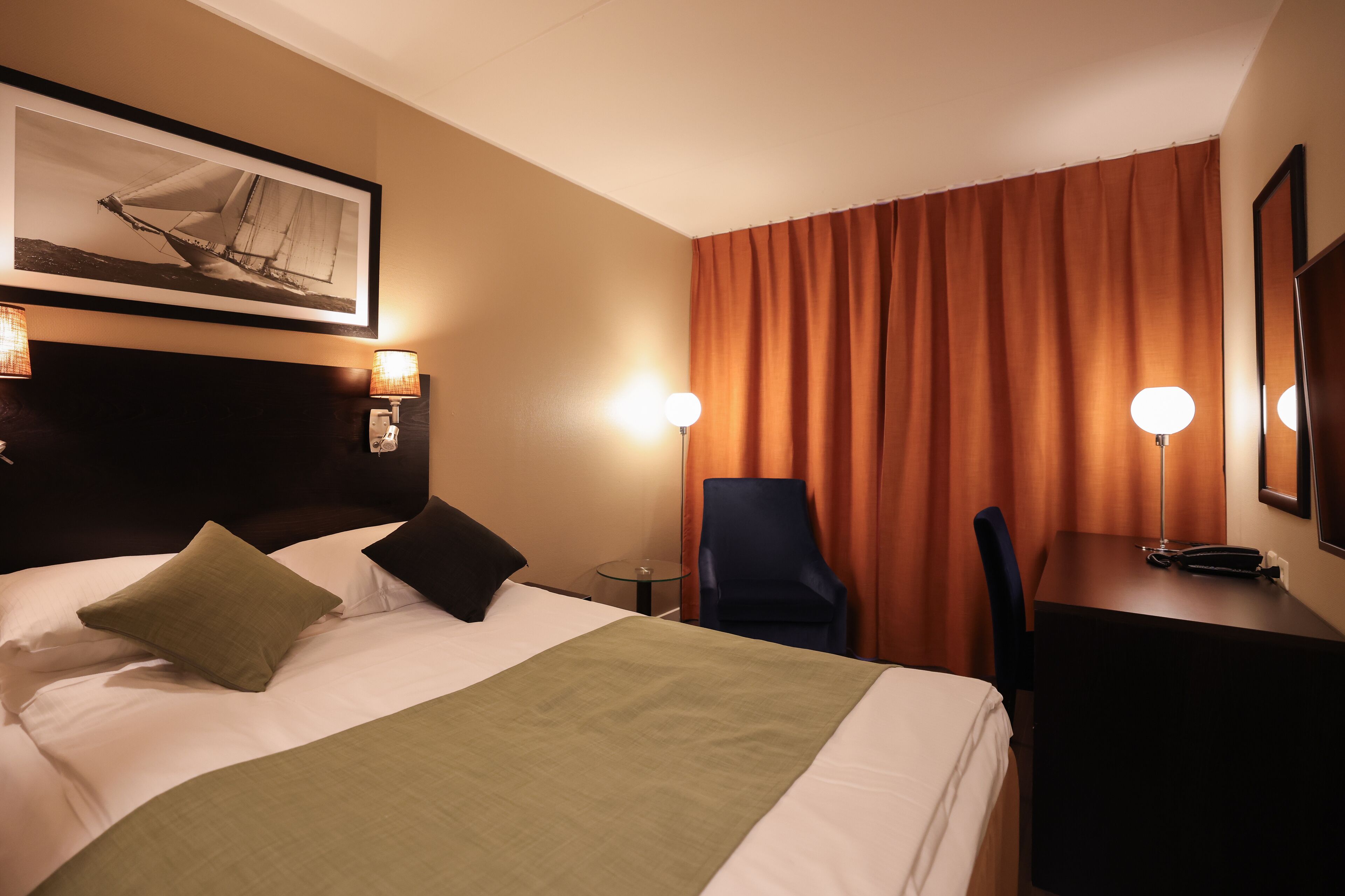 A hotel room with a bed, a desk, a chair, and a large window with curtains.