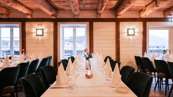 Uma sala de jantar com mesas preparadas para uma refeição, com um centro de mesa de velas e vista para o exterior.