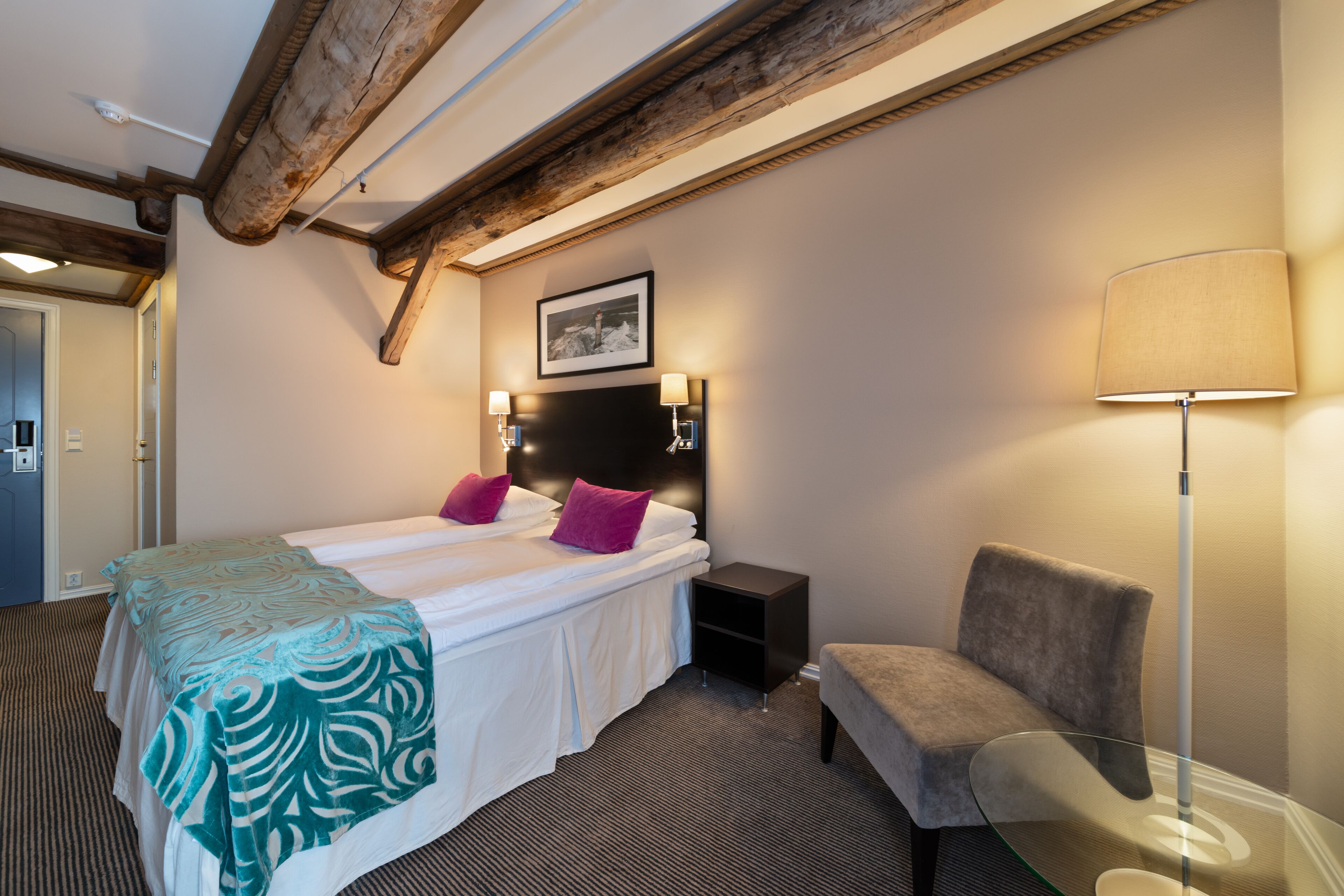 A hotel room with a bed, bedside lamps, a chair, and a picture on the wall.