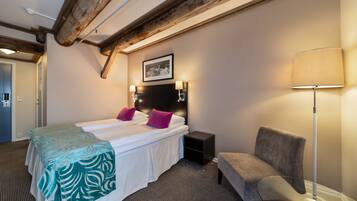 A hotel room with a bed, bedside lamps, a chair, and a picture on the wall.