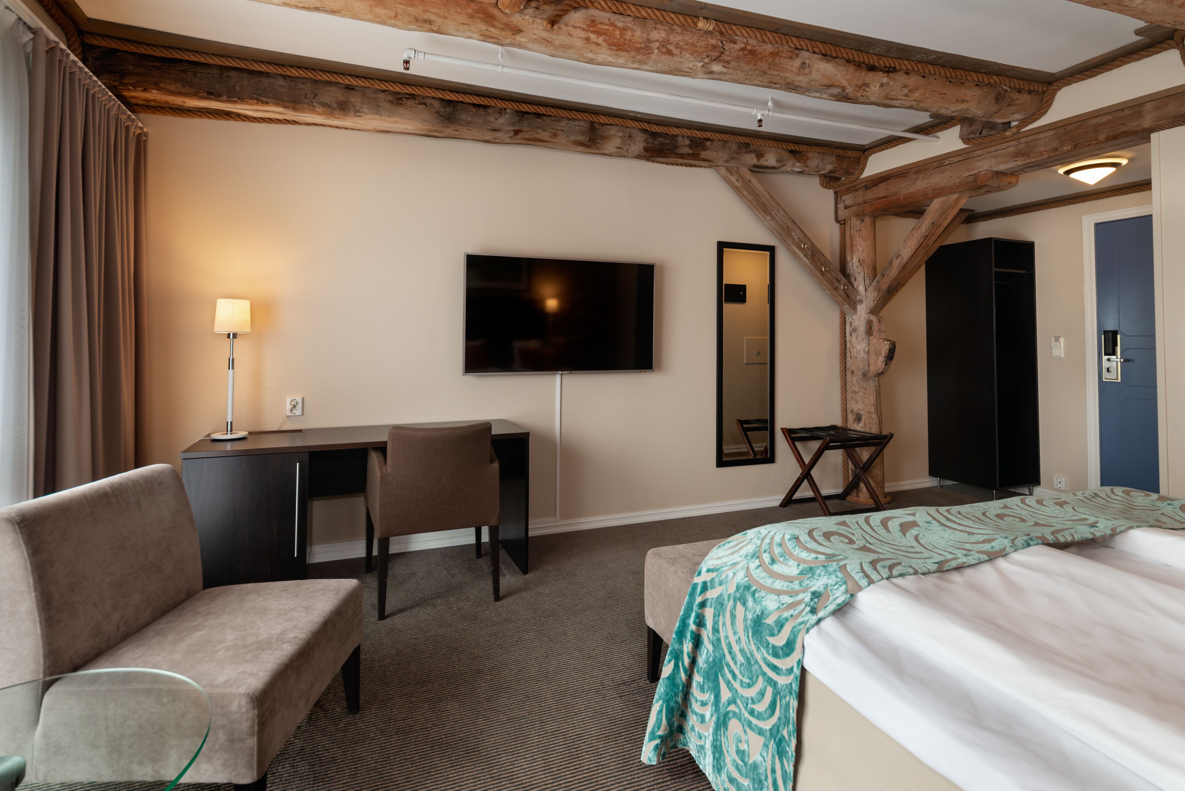A hotel room with a bed, a desk, a chair, a television, and a mirror.