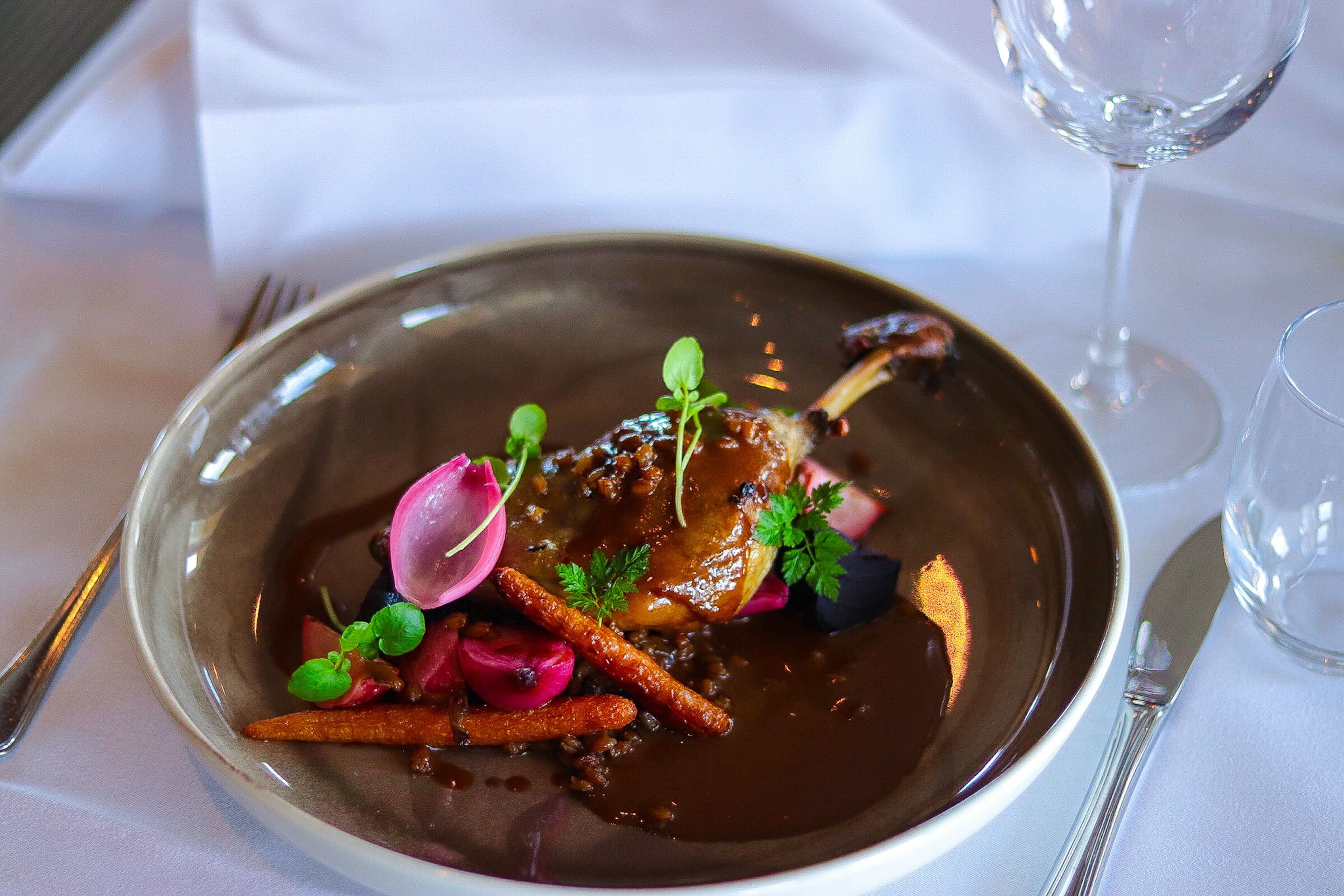 A plated dish with a variety of garnishes and a glass of wine on a table.