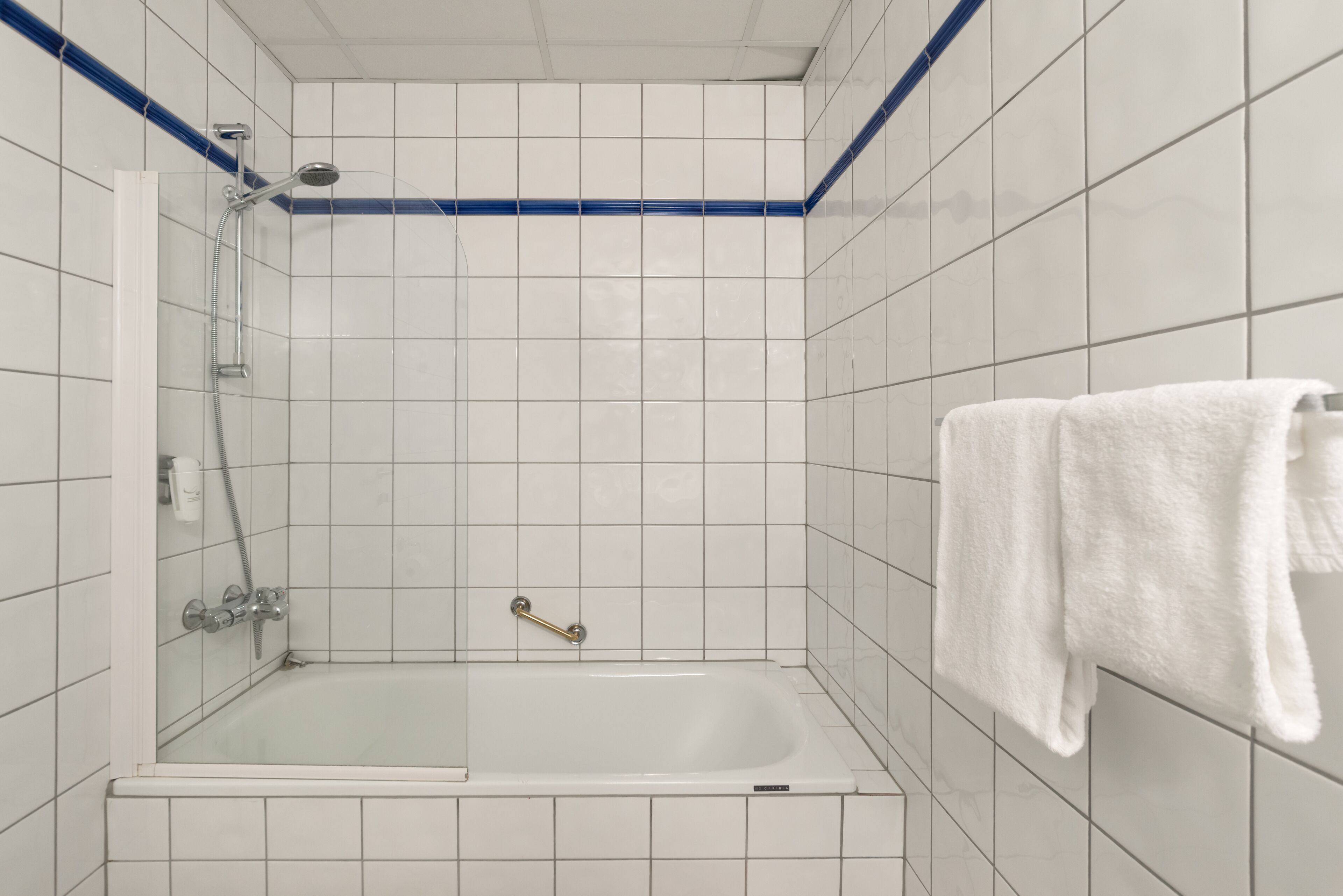 A bathroom with a white bathtub, a shower, and a towel hanging on the wall.
