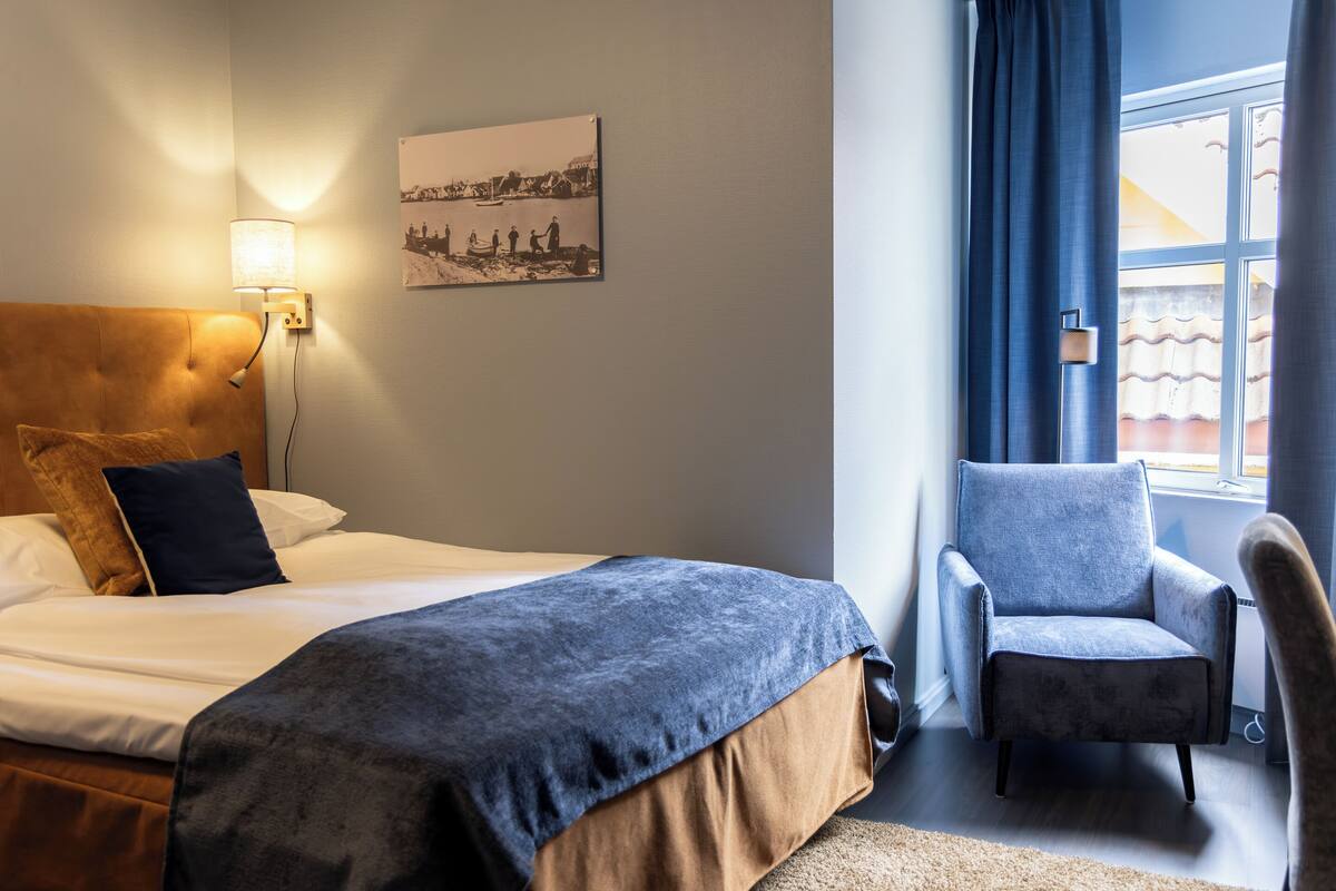 A hotel room with a bed, a chair, a lamp, and a picture on the wall.