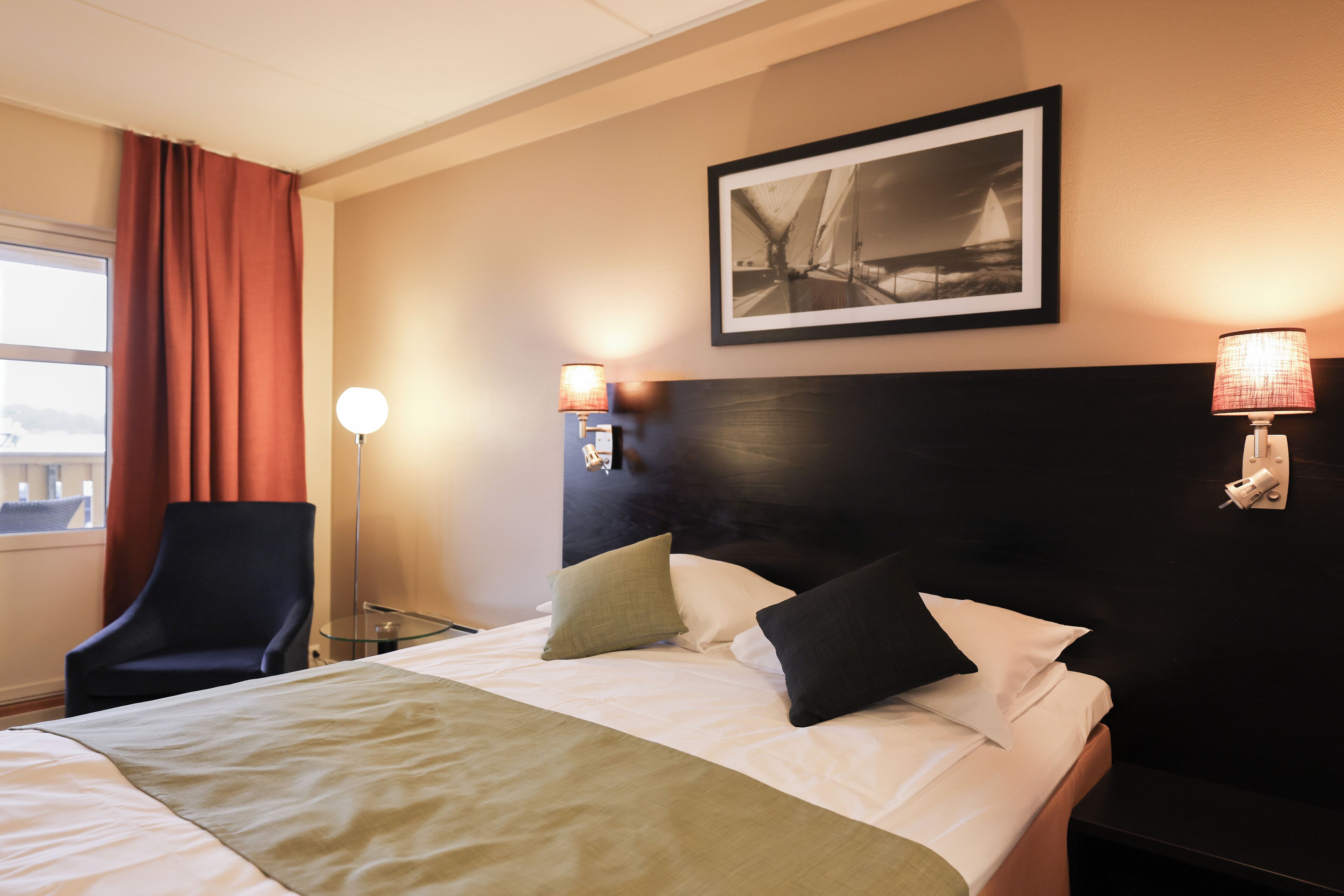 Ein Hotelzimmer mit Bett, Sessel, Schreibtisch und Lampe.