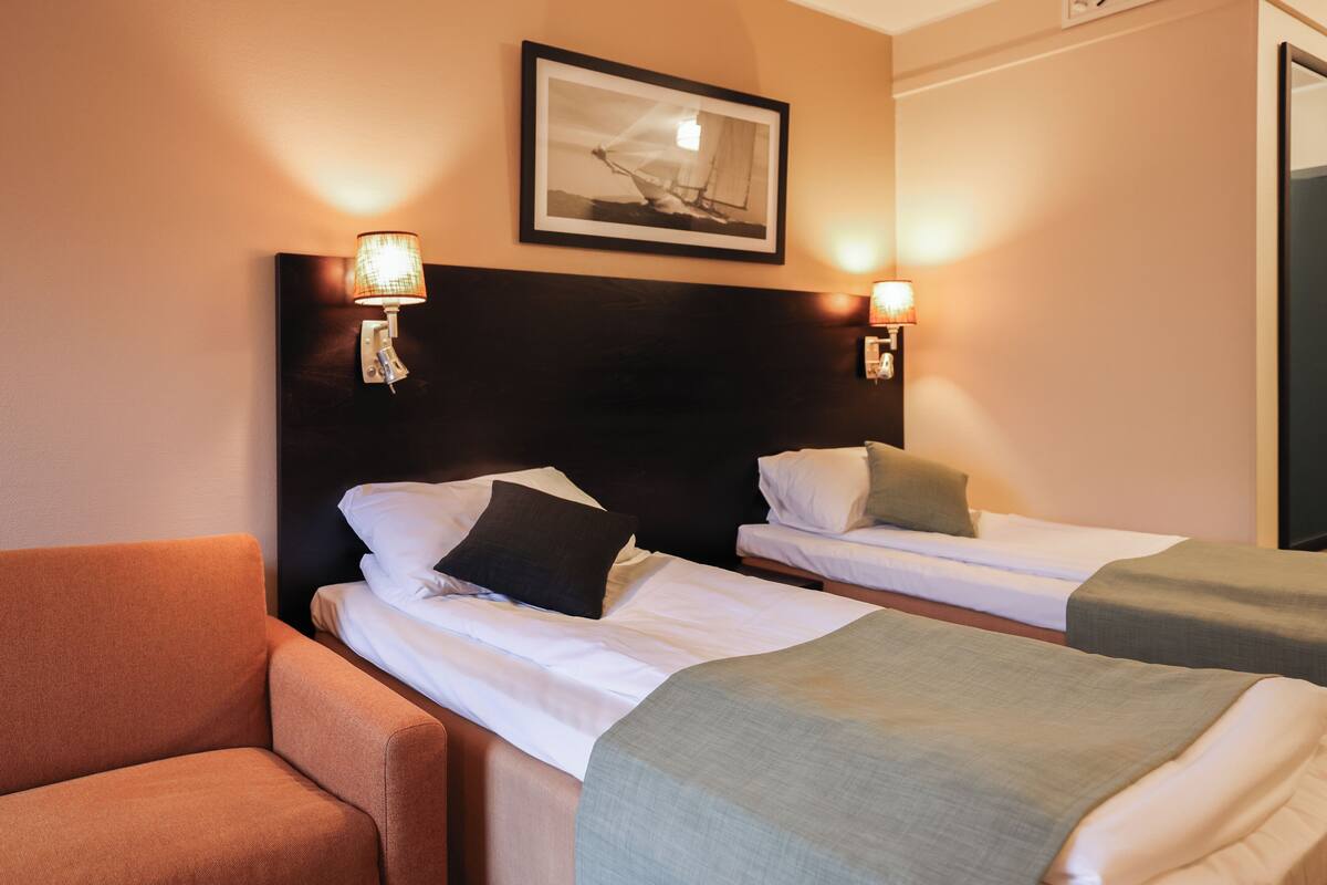 A hotel room with two single beds, a sofa, and a framed picture on the wall.