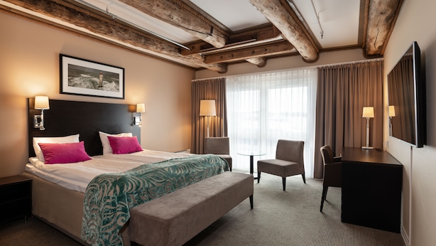 A hotel room with a large bed, a desk, a chair, and a small table.