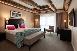 A hotel room with a large bed, a desk, a chair, and a small table.