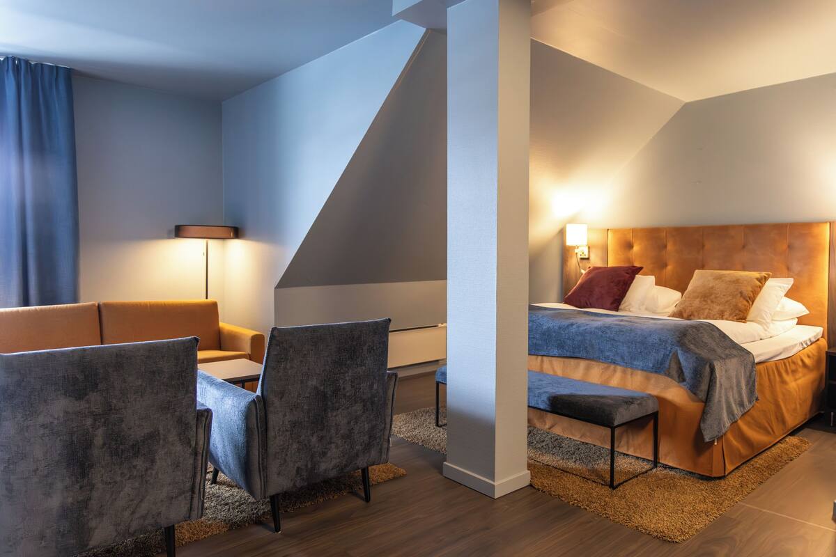 A modern hotel room with a bed, sofa, and chairs.