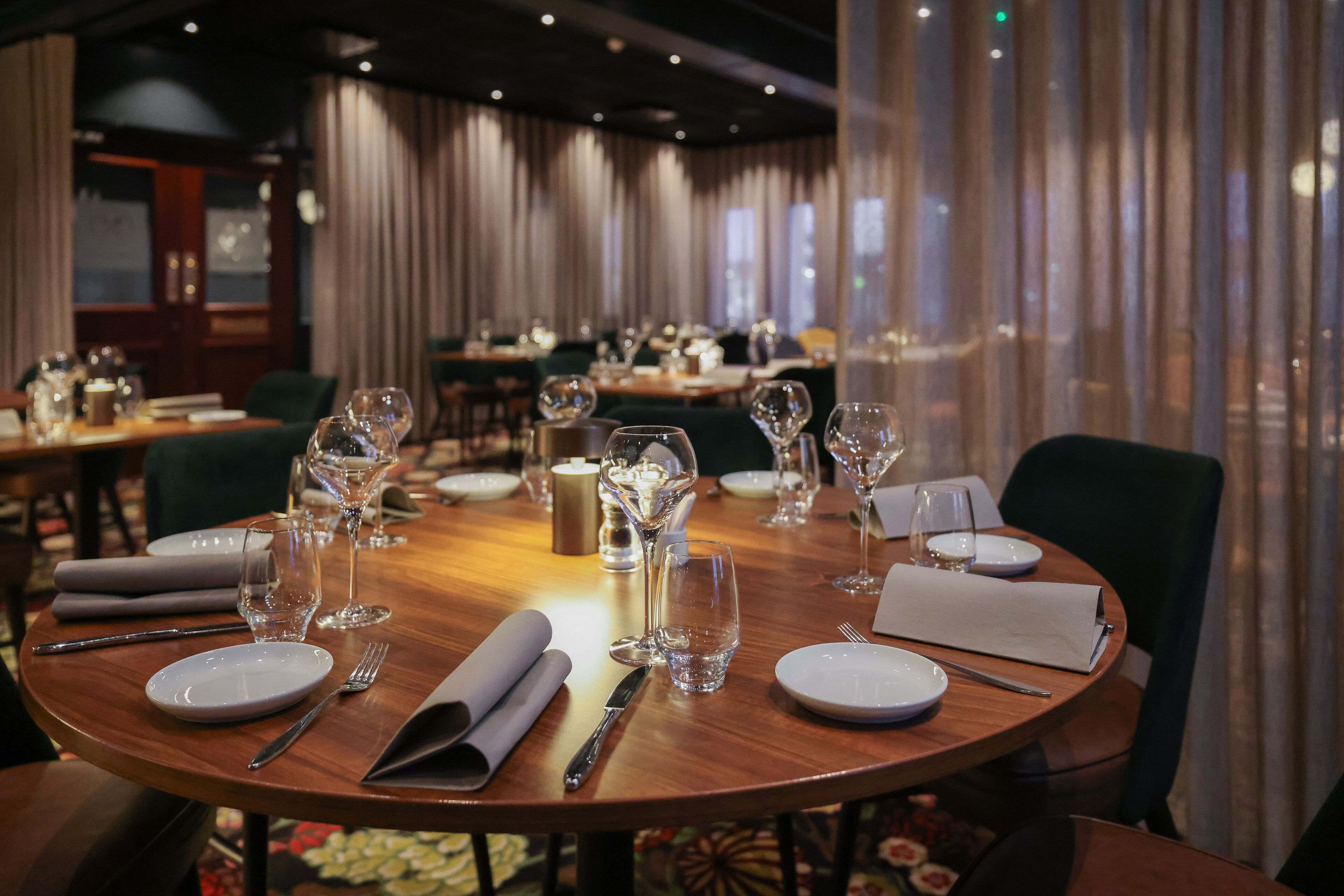 A dining area with round tables set for a meal, complete with plates, cutlery, and wine glasses.