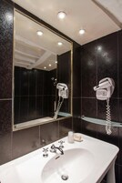 A bathroom with a white sink, two hair dryers mounted on the wall, and a mirror with a gold frame.