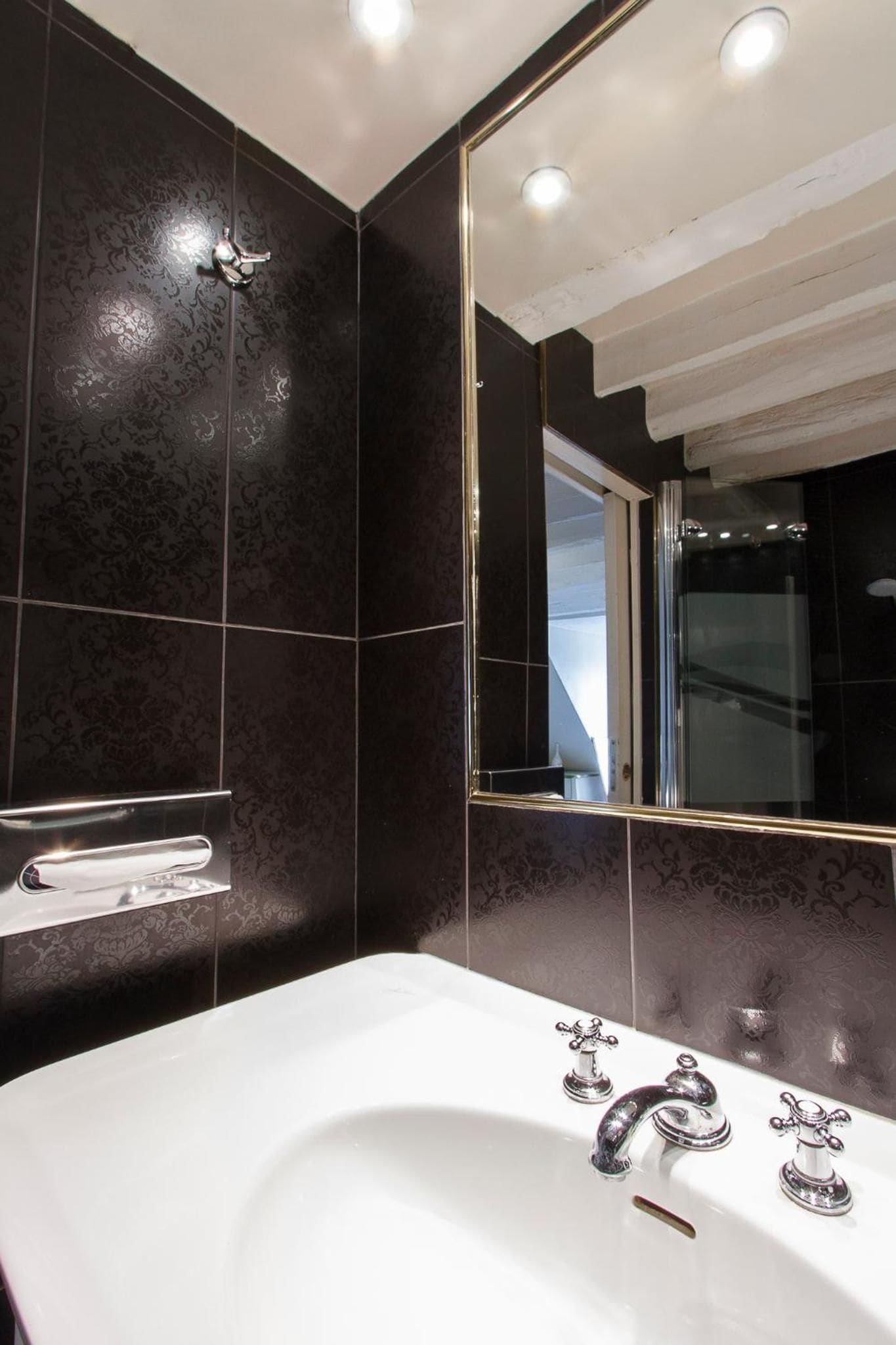 Une salle de bain moderne avec un grand miroir, des carreaux à motifs foncés et une baignoire blanche.