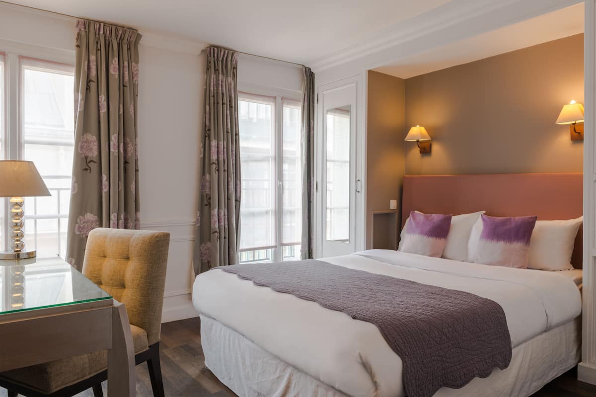 Una habitación de hotel con cama, una silla, un escritorio y una lámpara.