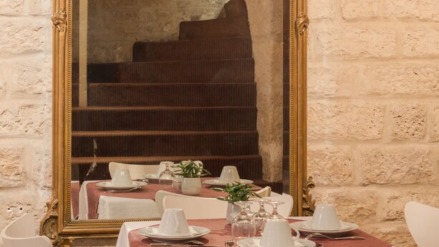 A dining area with a large ornate mirror, stone walls, and a staircase in the background. - Hôtel Gaillon Opéra (Paris)