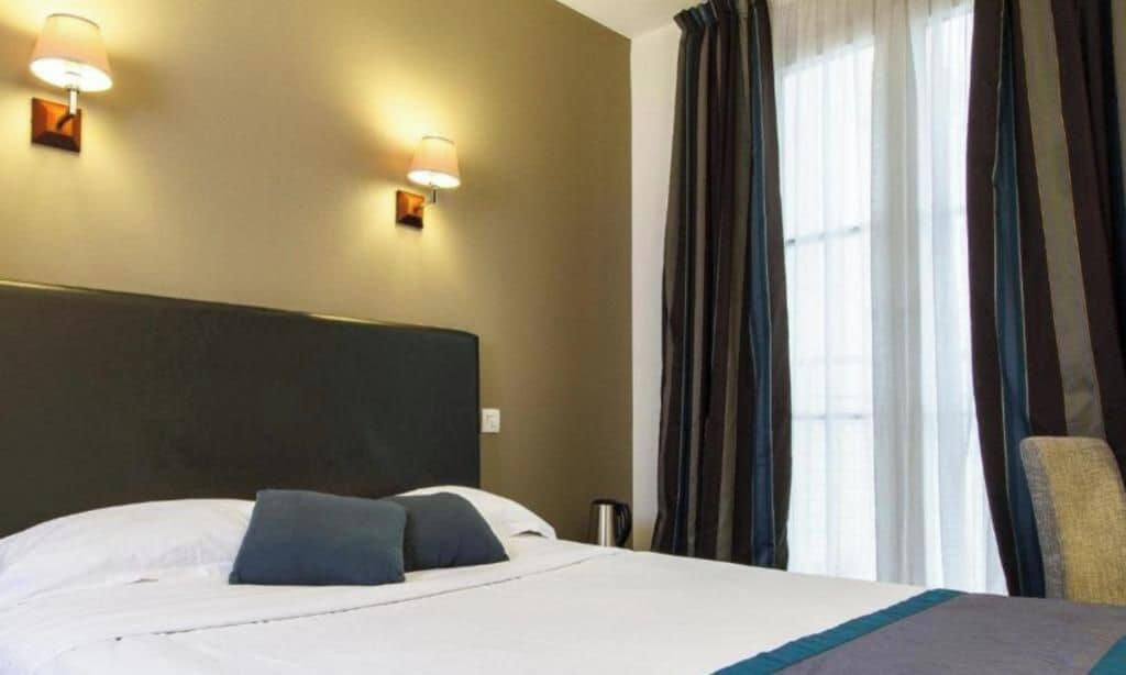 Ett hotellrum med en säng, två väggmonterade lampor, en stol och gardiner.